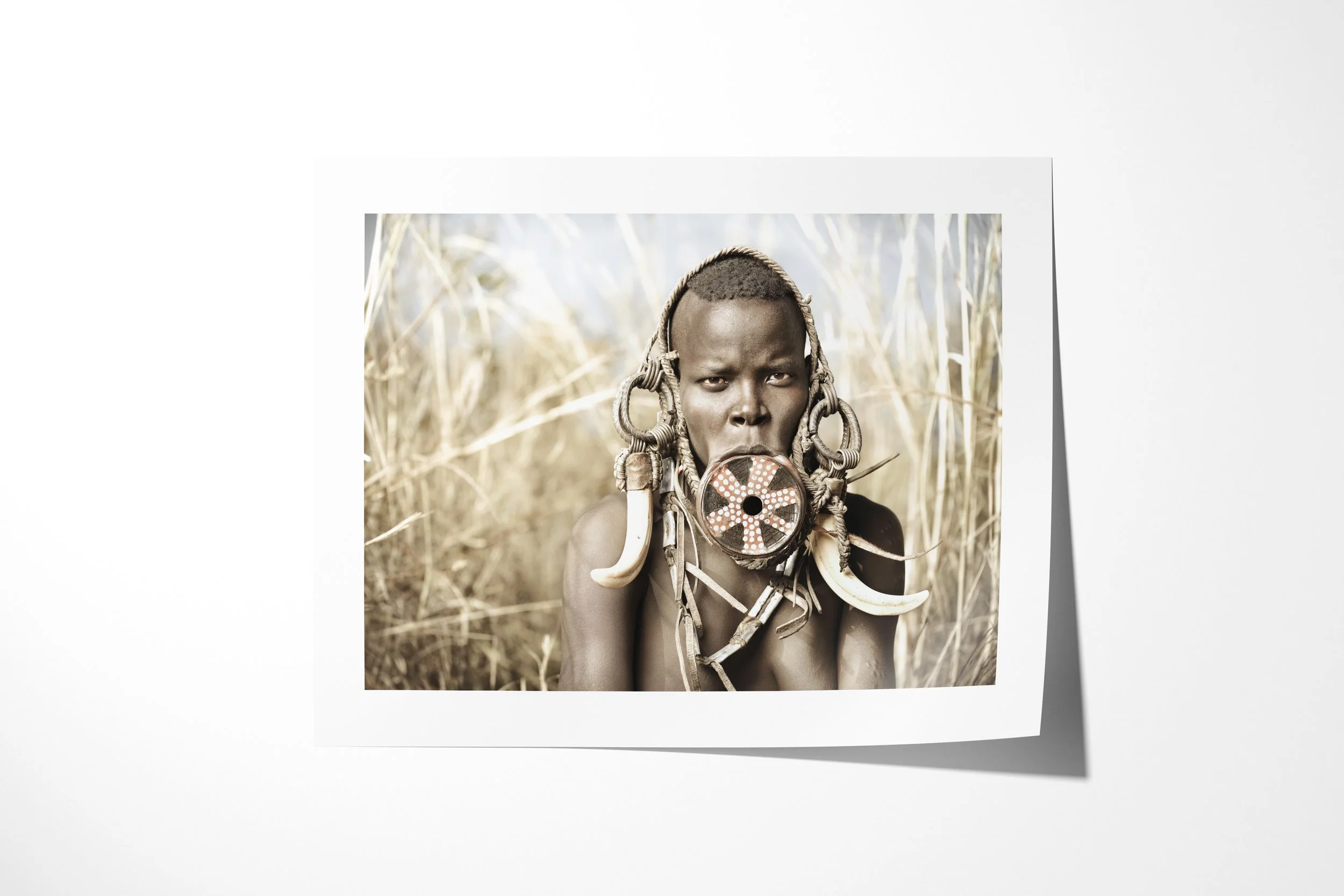 Fine art paper print of Uluio, showing a close portrait of a Mursi woman wearing a painted lip plate, large tusks and layered ornaments.