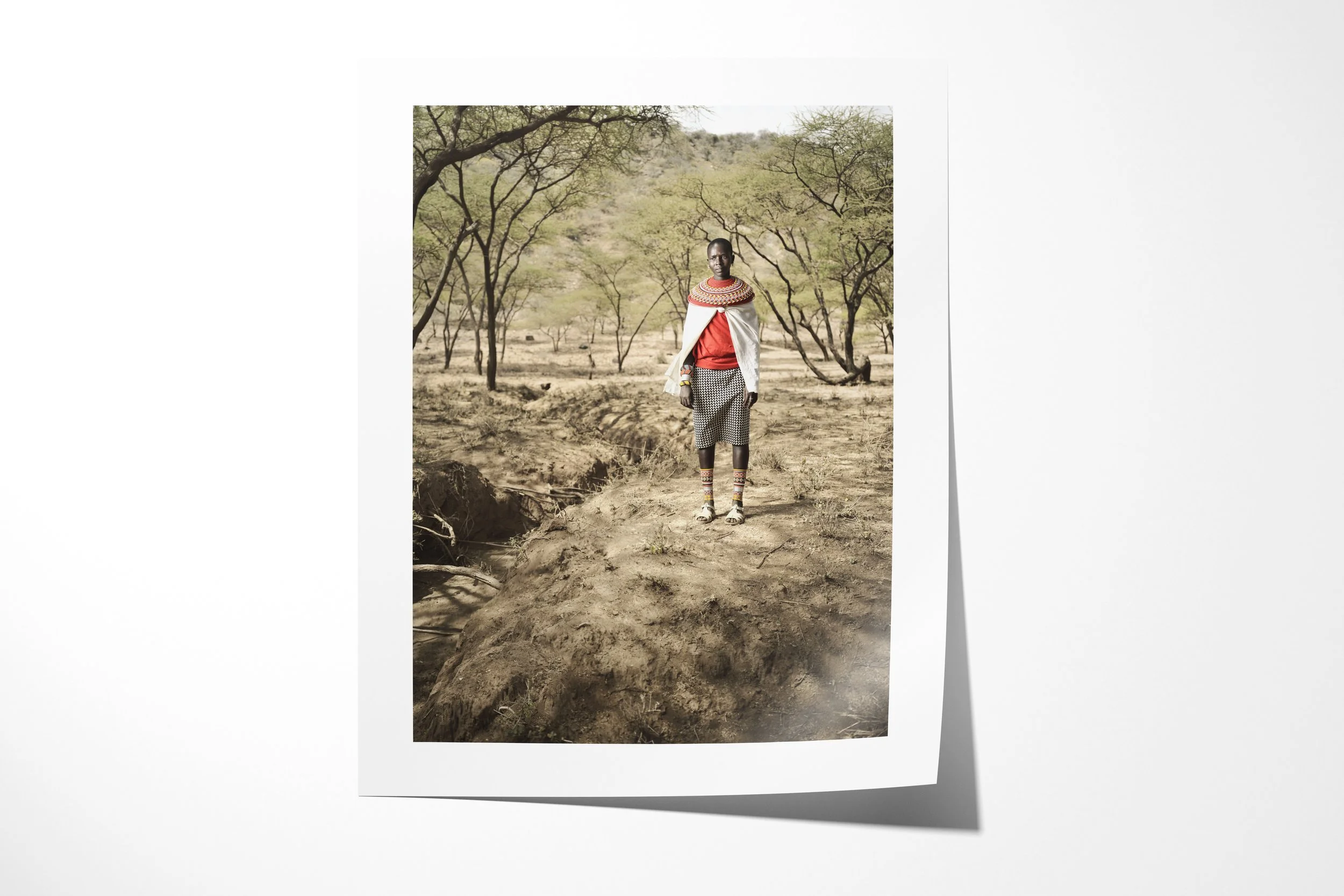 Fine art paper print of Noswuray, showing a Samburu woman wearing a white shawl and broad bead collar on a path through open woodland.