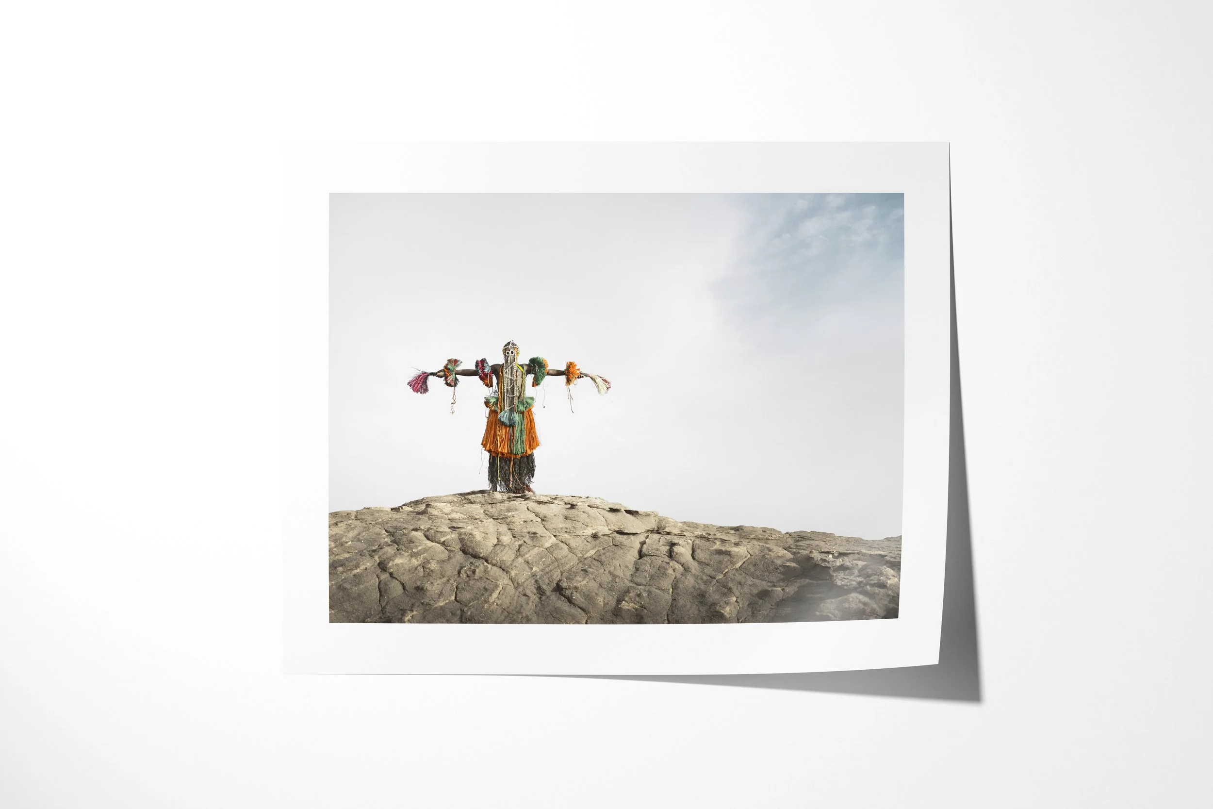 Fine art paper print of Legada Iyayi (Mask), showing a Dogon bird mask with outstretched arms standing on a rock ridge.