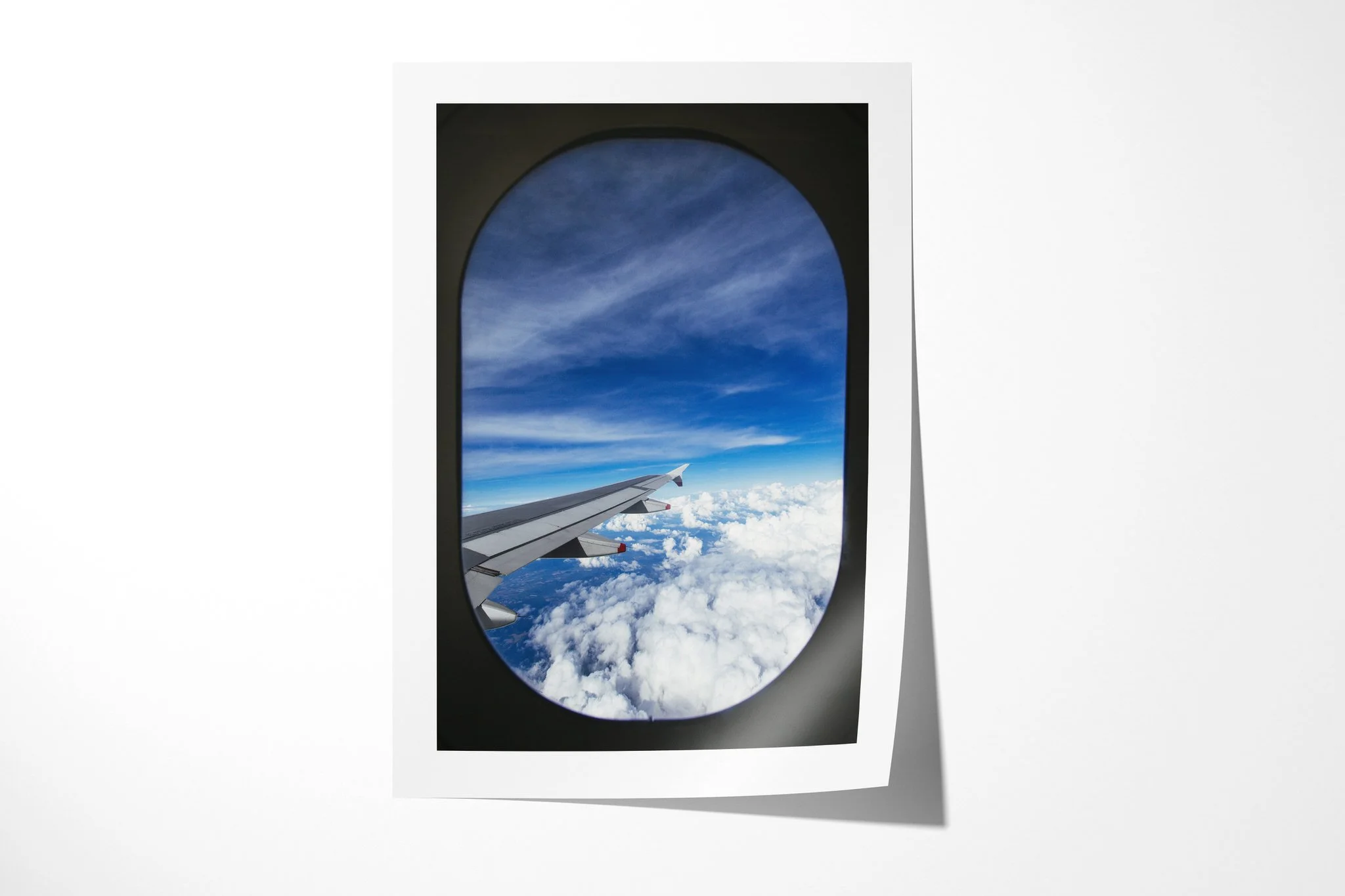 Unframed fine art paper print of Room With A View, showing an aircraft wing above bright cloud tops and deep blue sky, framed by the dark oval of a passenger window.
