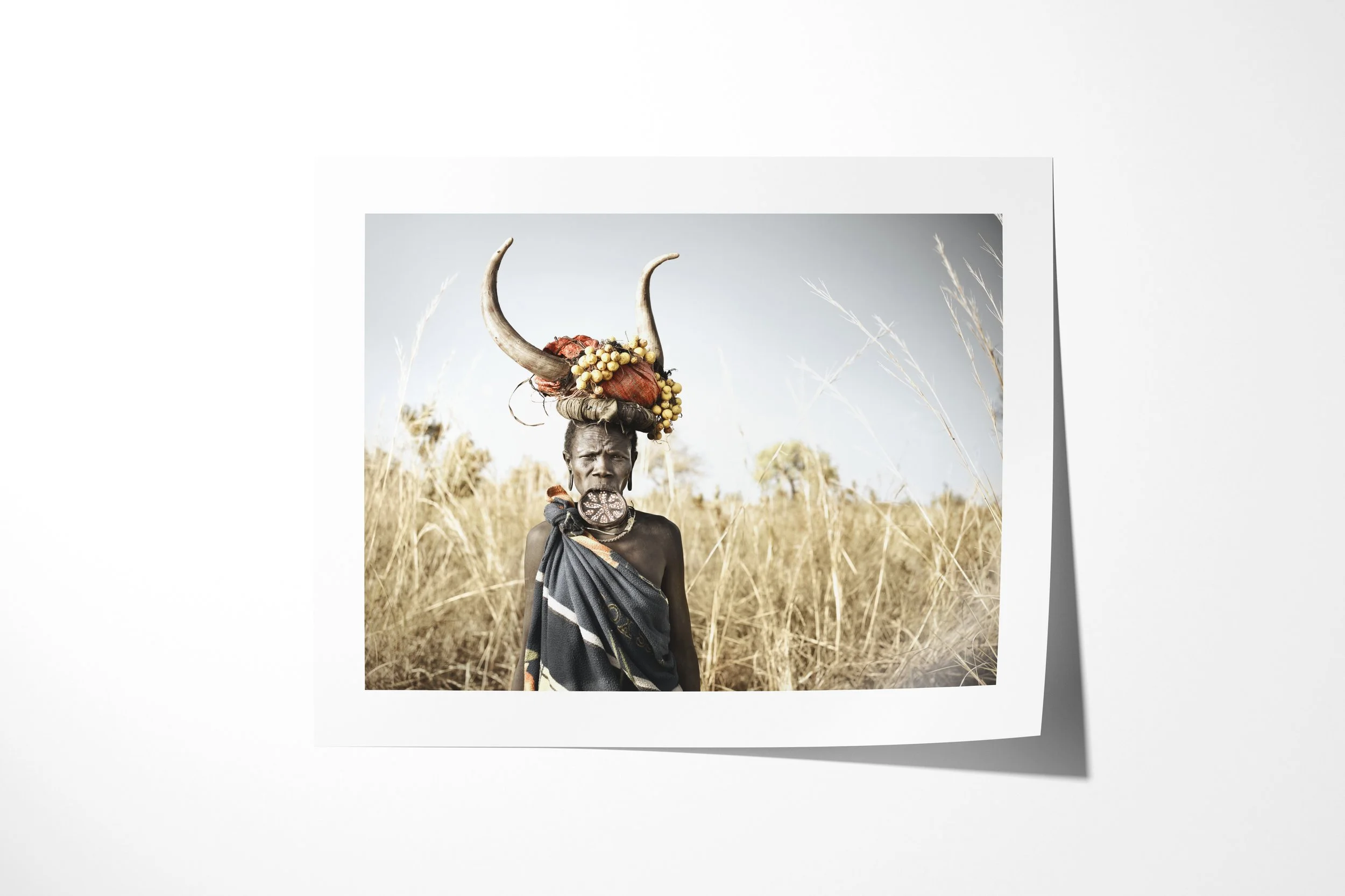 Fine art paper print of Makune, showing a Mursi woman wearing a decorated lip plate and curved-horn headdress in tall grass.