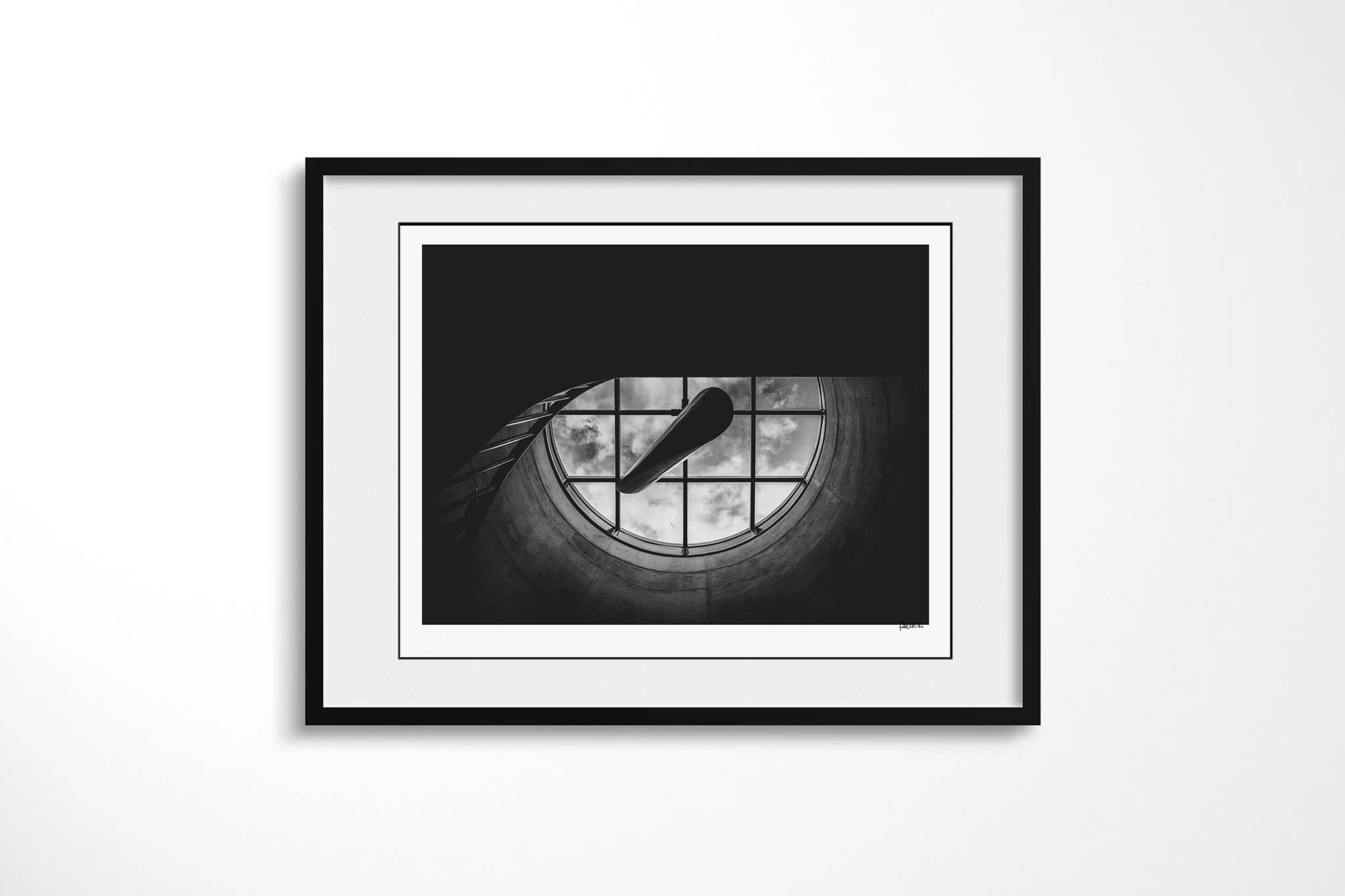 Framed fine art presentation of Skylight in a black frame with a white mount, depicting a circular concrete skylight with a window grid and clouds, crossed by two dark blade-like architectural forms.