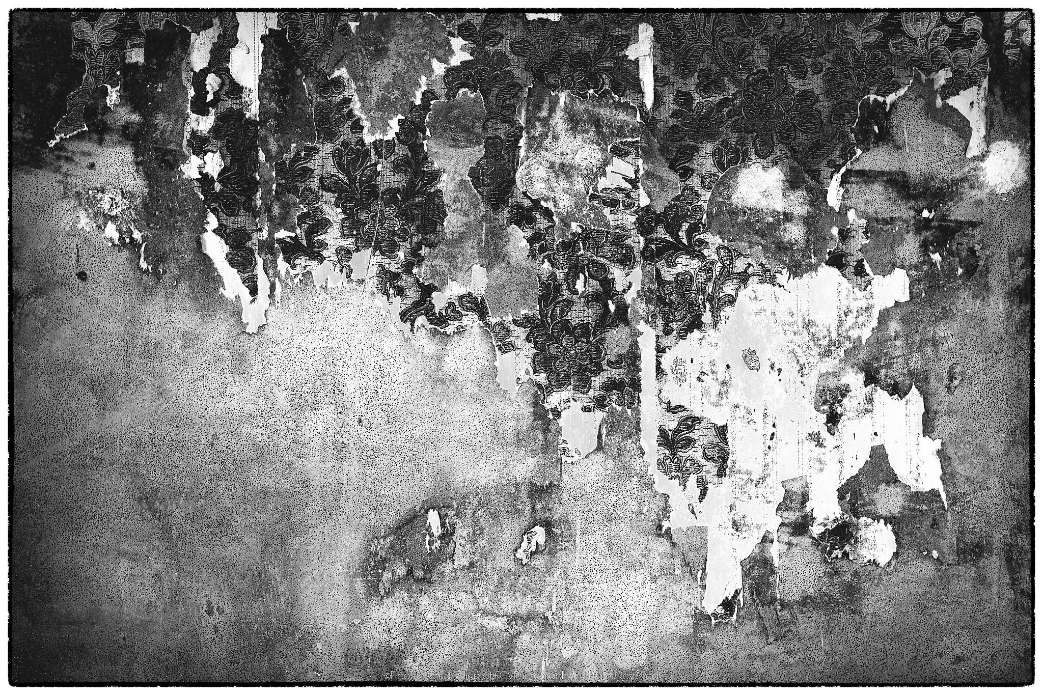 Weathered wall surface with pale peeling layers exposing dark floral patterning beneath.