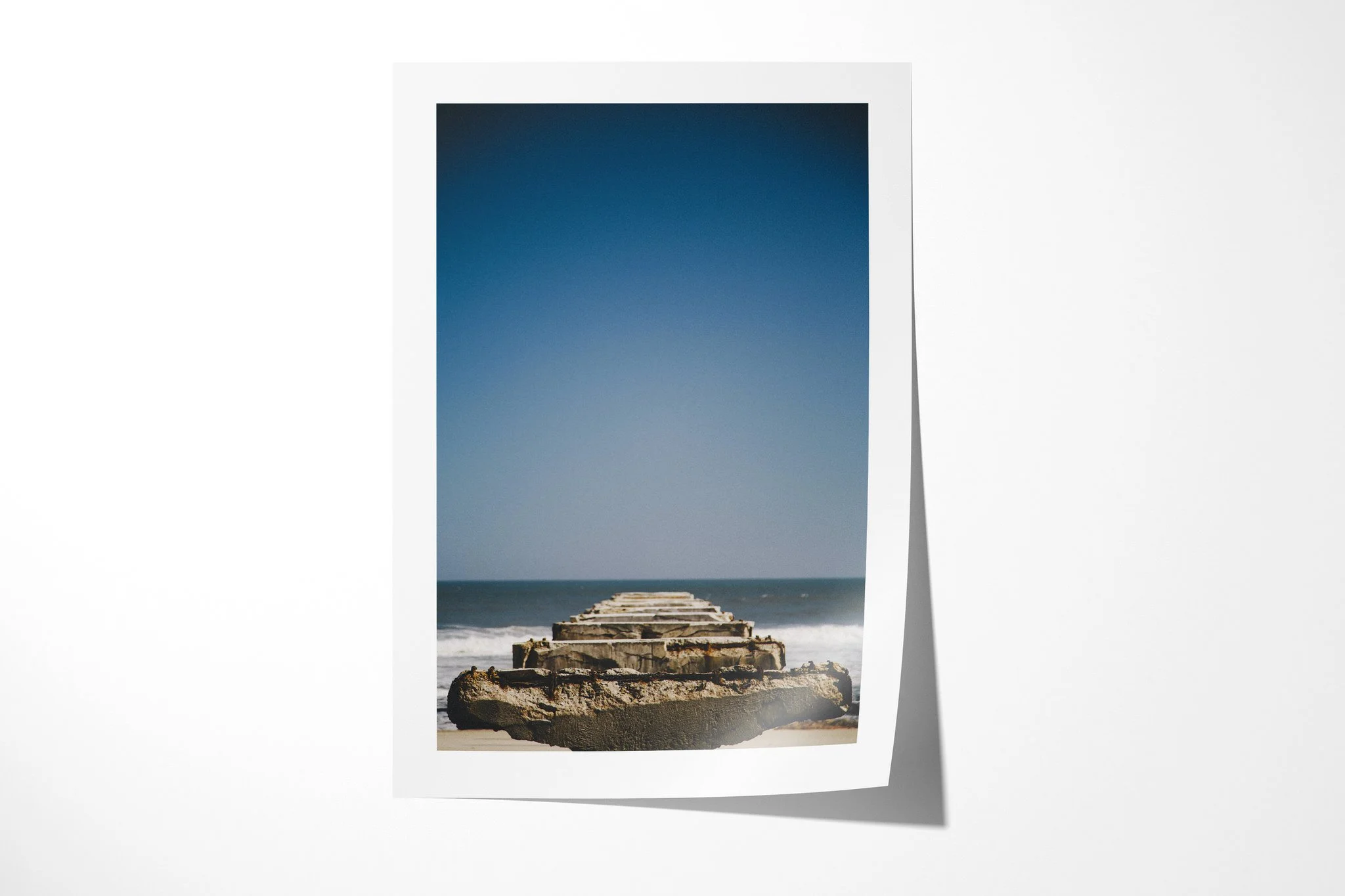 Unframed fine art paper print of Skeleton Coast, showing crumbling concrete remnants extending from sand into the Atlantic surf on Namibia's Skeleton Coast.