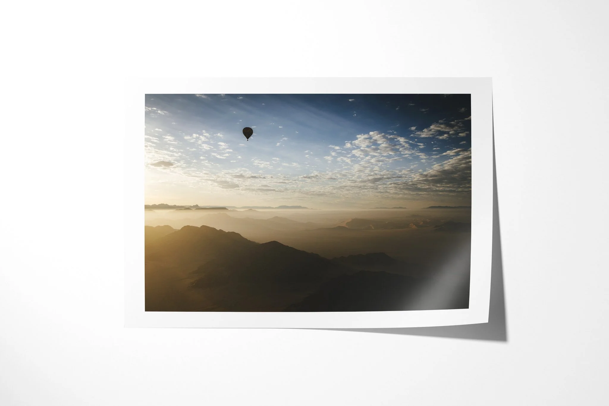 Fine art paper print of 80 Days, showing a lone hot-air balloon above layered arid mountain ridges in warm early light beneath scattered clouds.