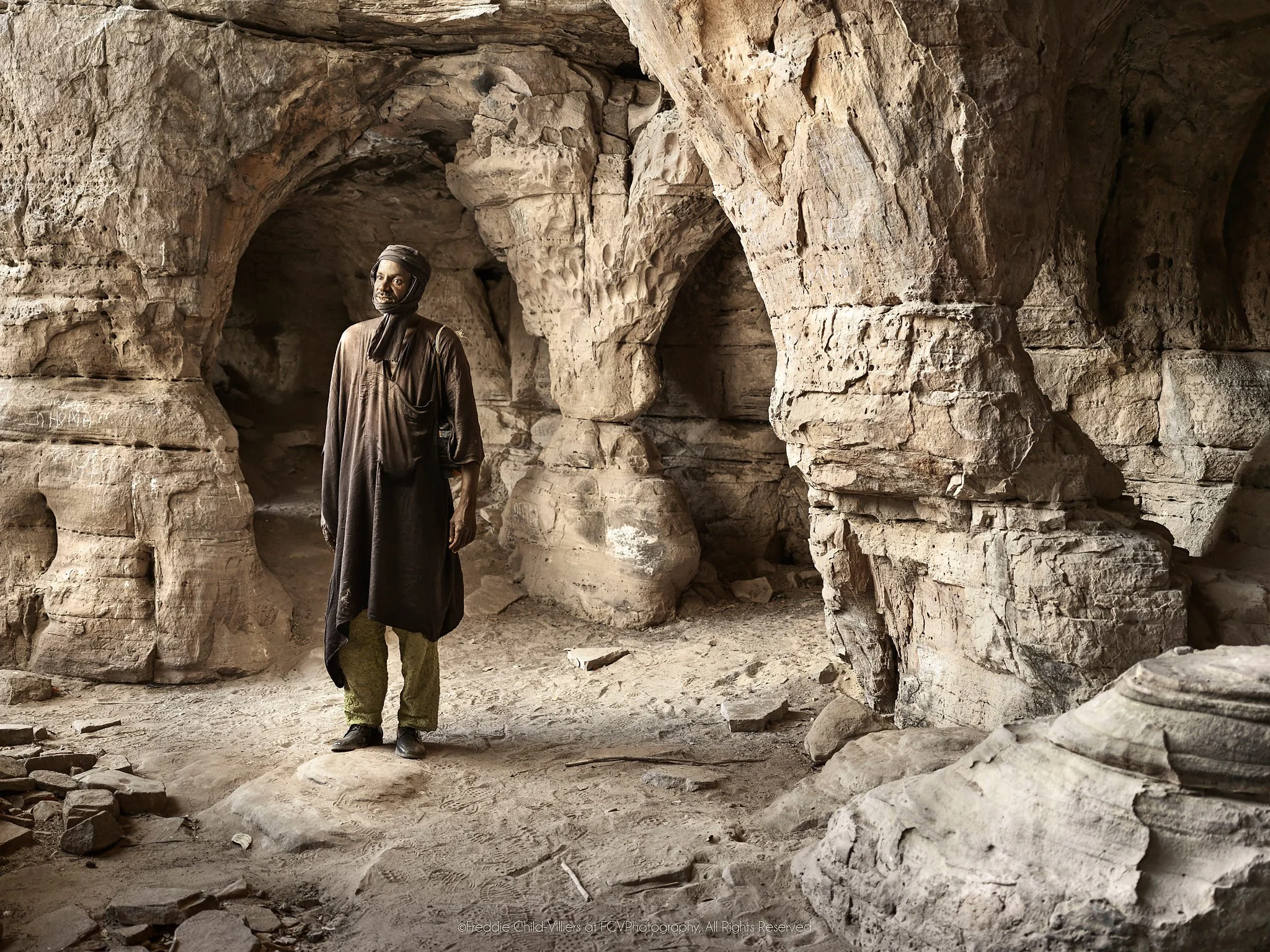 Alou standing within the carved arches and columns of a sandstone cave.