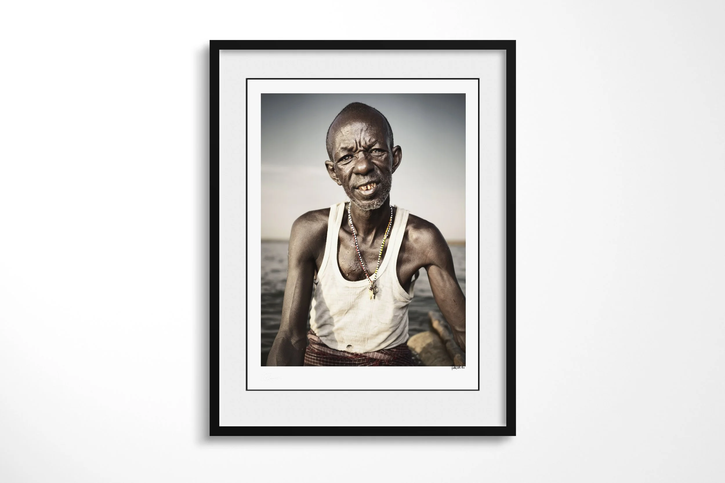 Framed presentation of Lengutuk in a black frame and white mount, showing a close portrait of an older El Molo fisherman beside the waters of Lake Turkana.