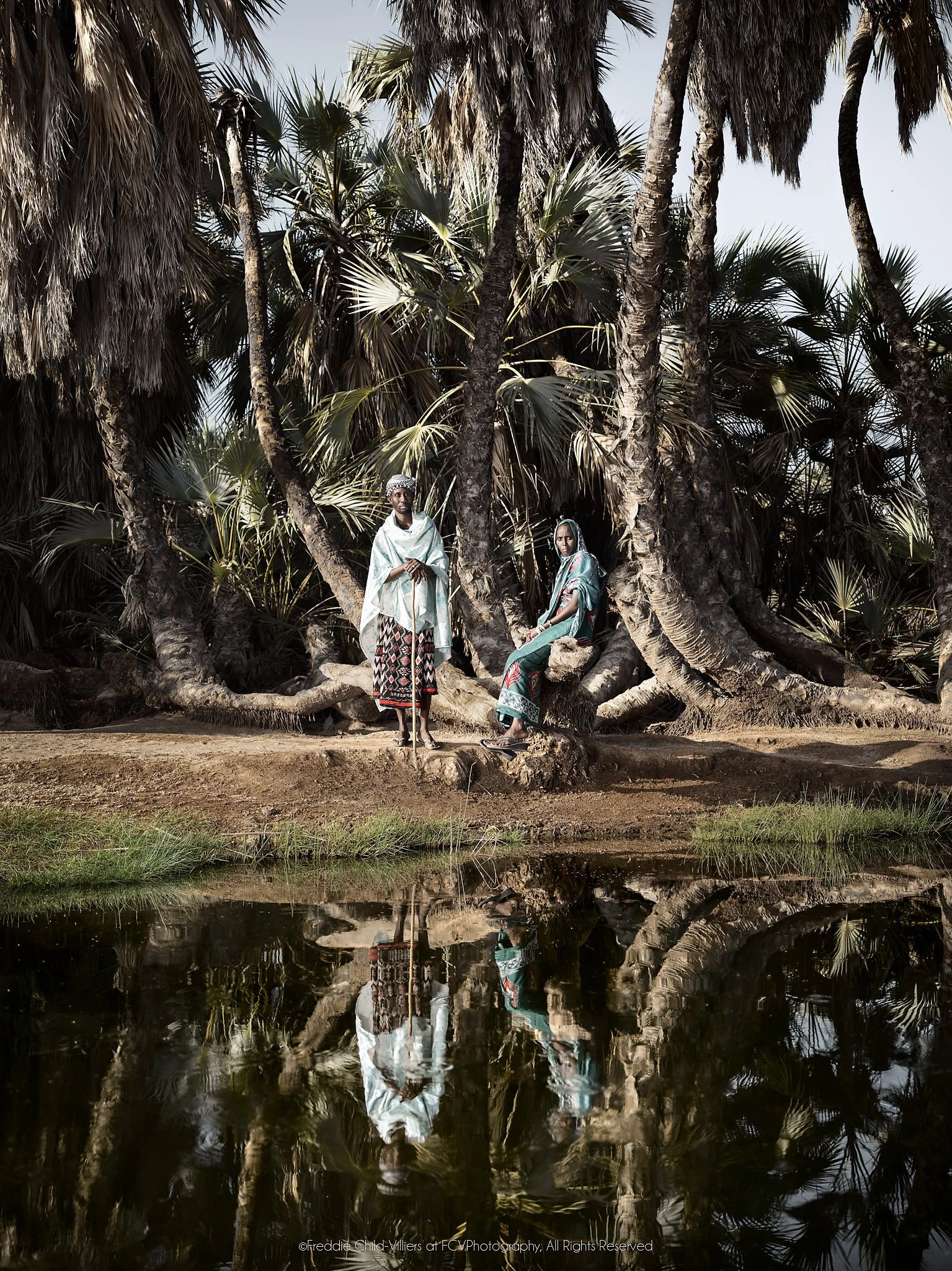 Talaso and Halkano standing beside a still spring among dense doum palms.