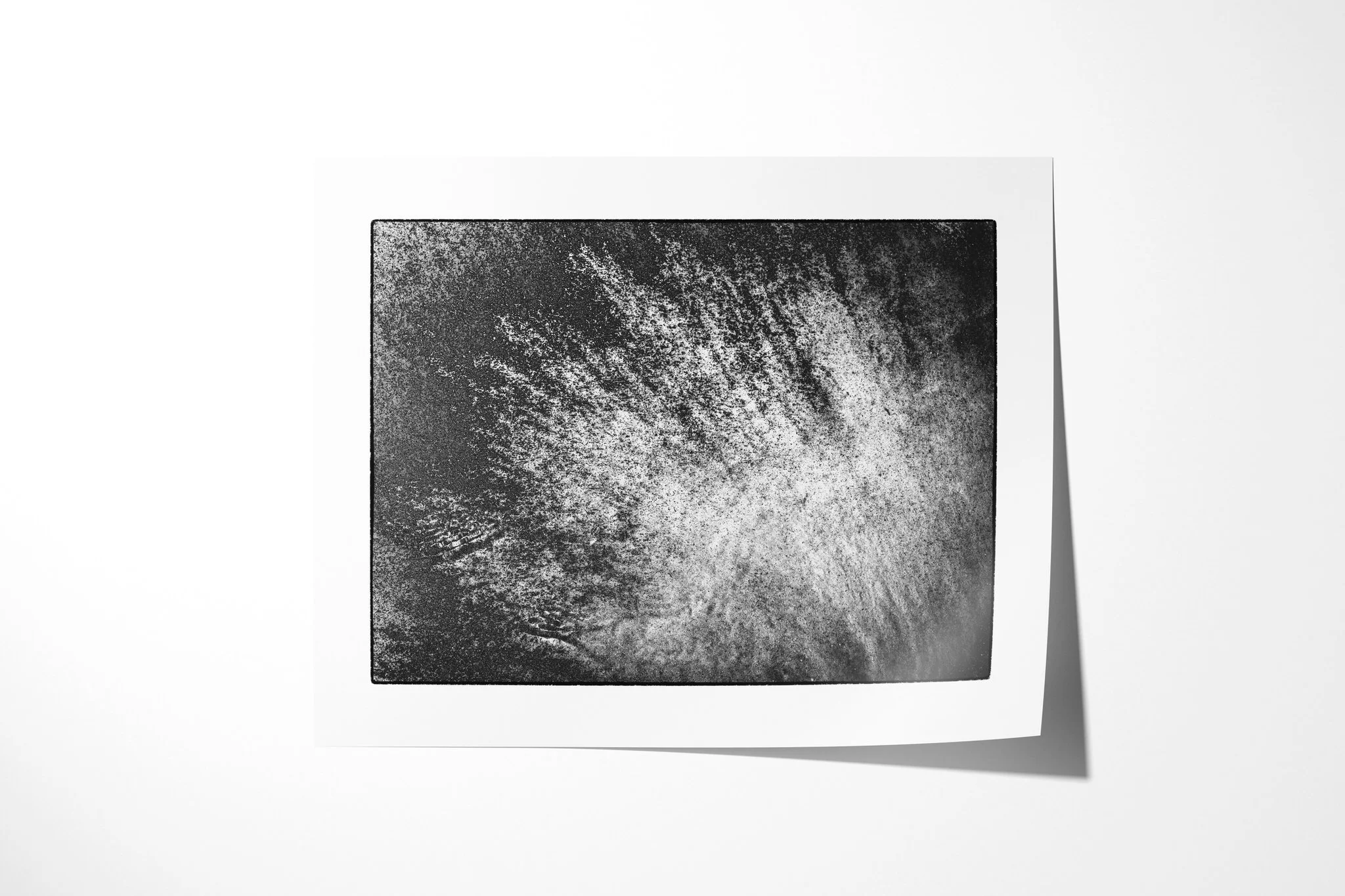 Unframed fine art paper print of Manganese II, featuring a bright fan of fine radiating streaks spreading diagonally across a dark granular surface.