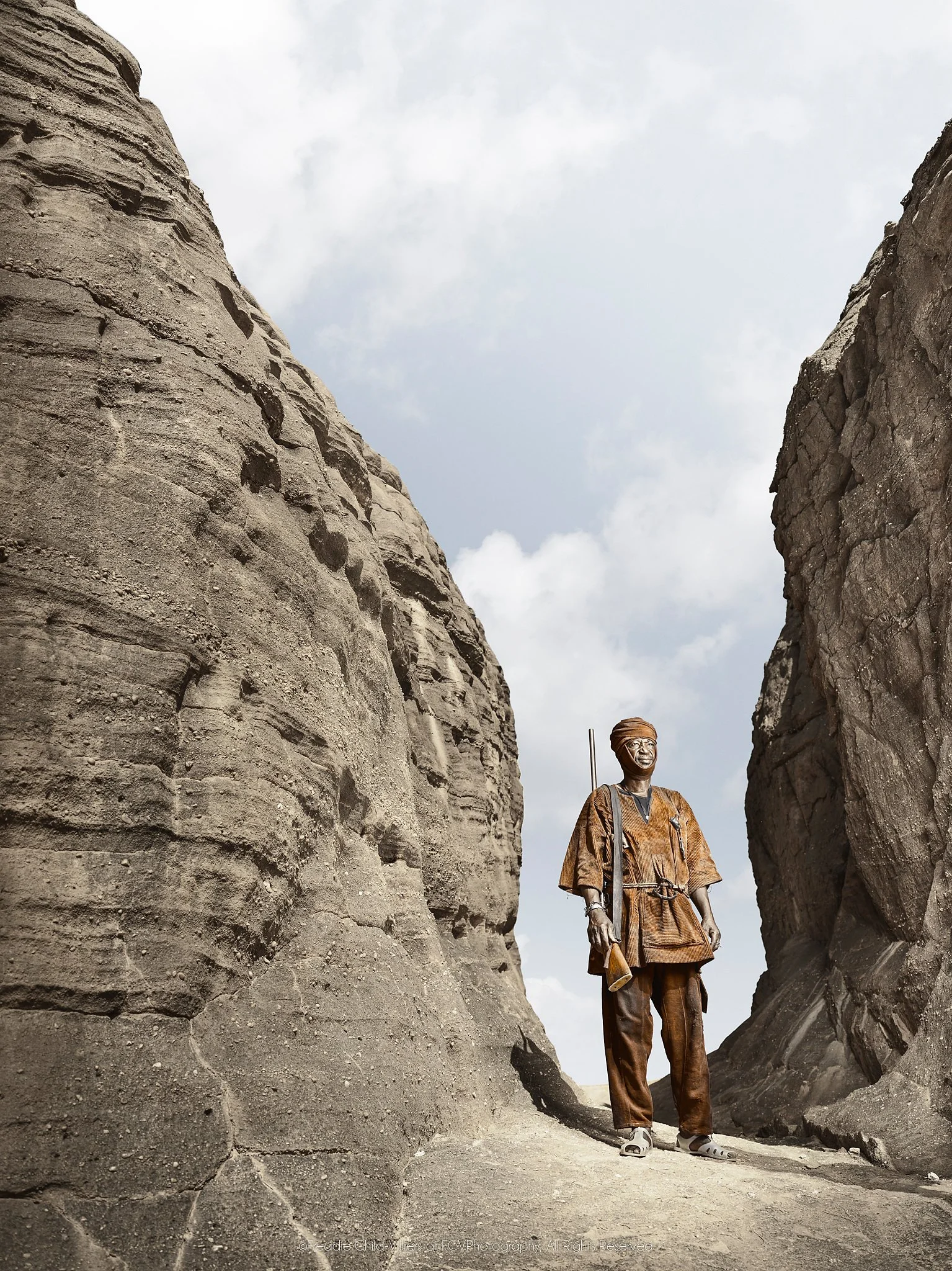 Jean standing between towering sandstone walls in a narrow mountain passage.