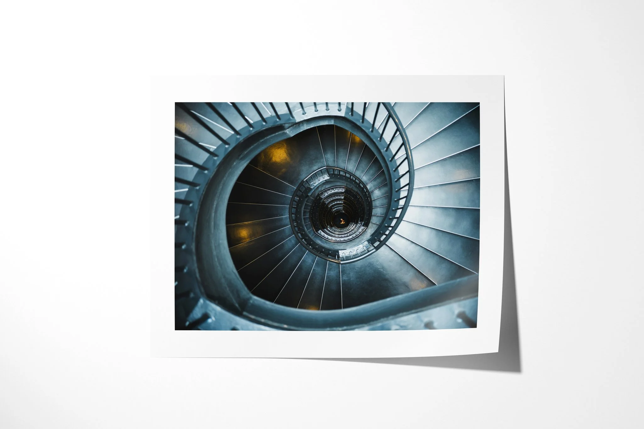 Spiral presented as an unframed fine art paper print, depicting a teal-blue spiral staircase viewed from above, tightening around a deep central void with small amber lights.