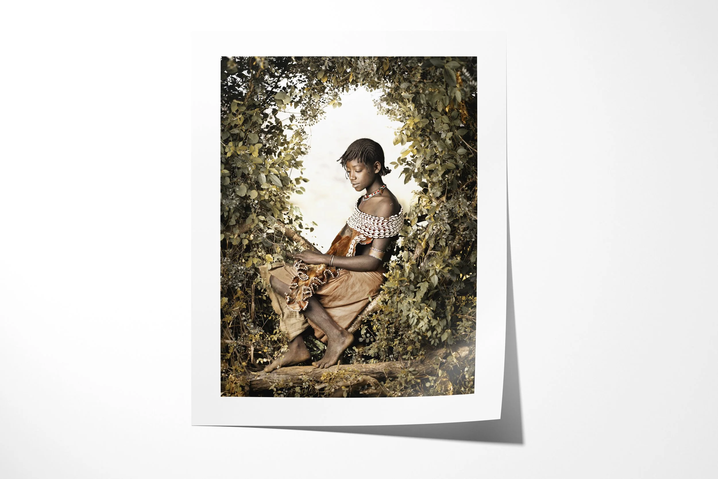 Fine art paper print of Semba, showing a young Banna woman seated in foliage wearing layered beadwork and a cowrie-covered leather garment.