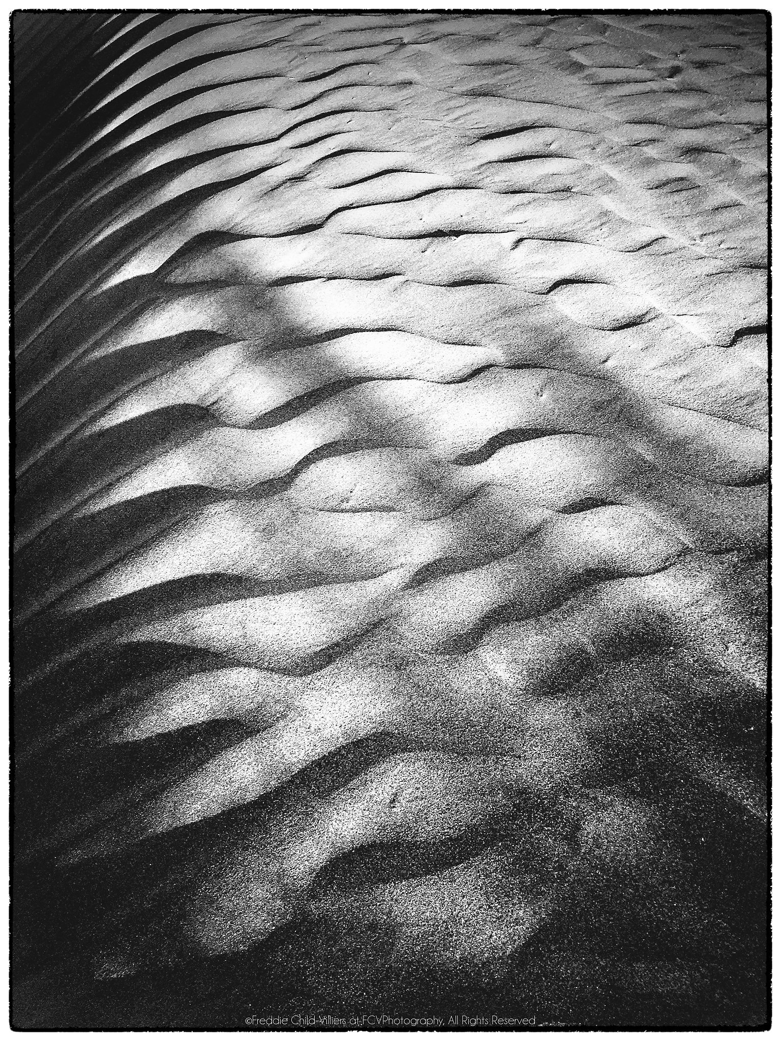Close view of sand ripples with bright crests and deep shadows fading towards the top.