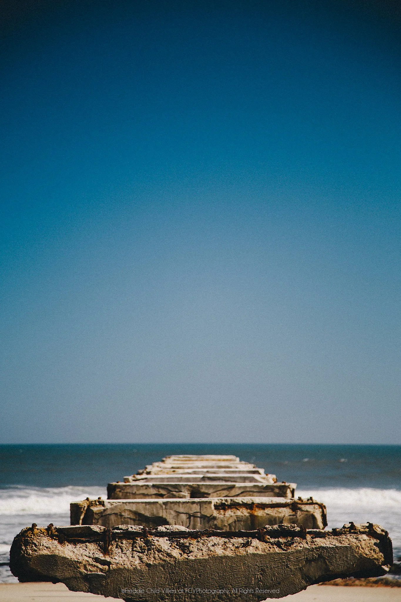 Crumbling concrete remnants extending from sand into the Atlantic surf on Namibia's Skeleton Coast.