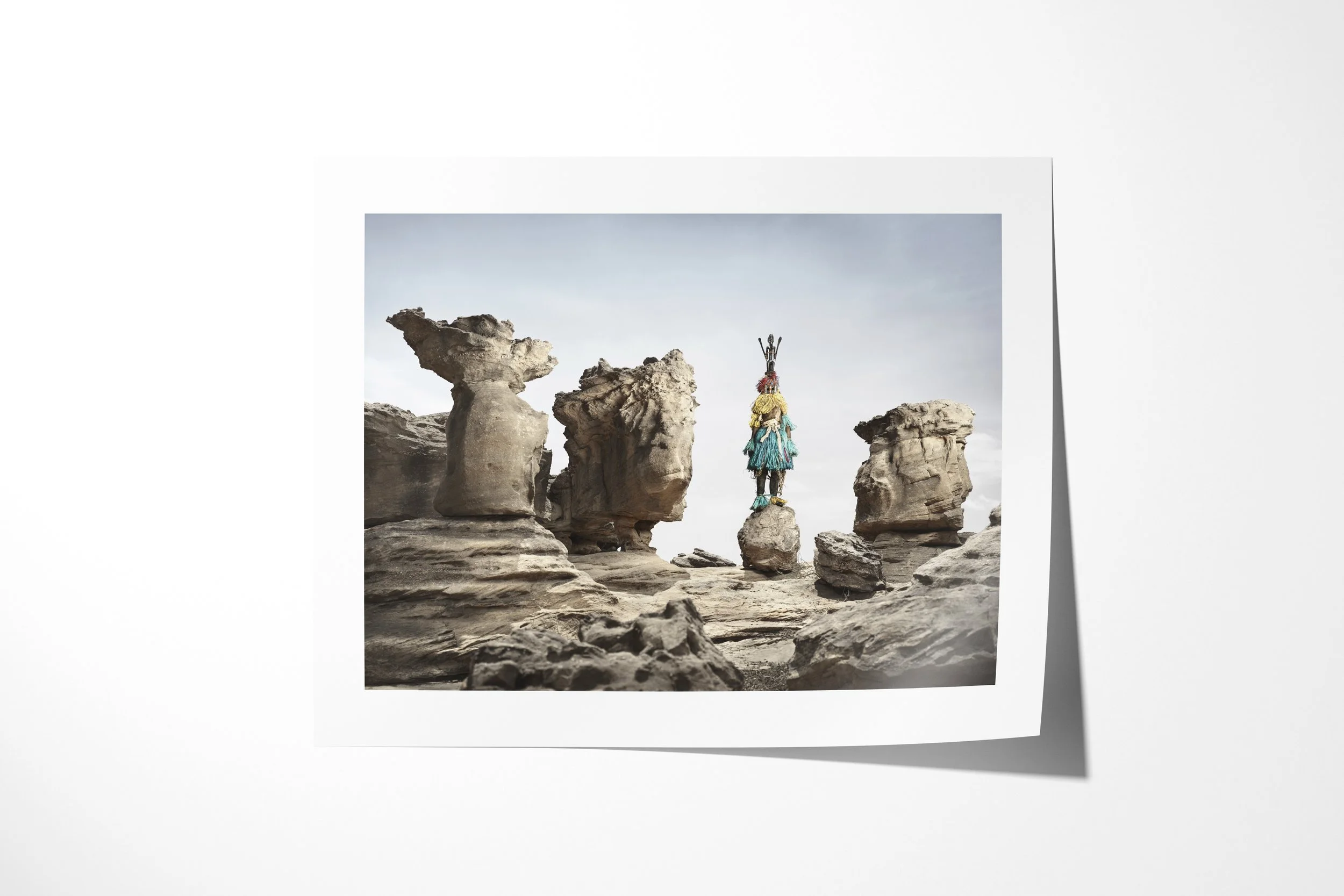 Fine art paper print of Satimbe (Mask), showing a Dogon Satimbe mask balanced on a small rock among weathered stone pillars.