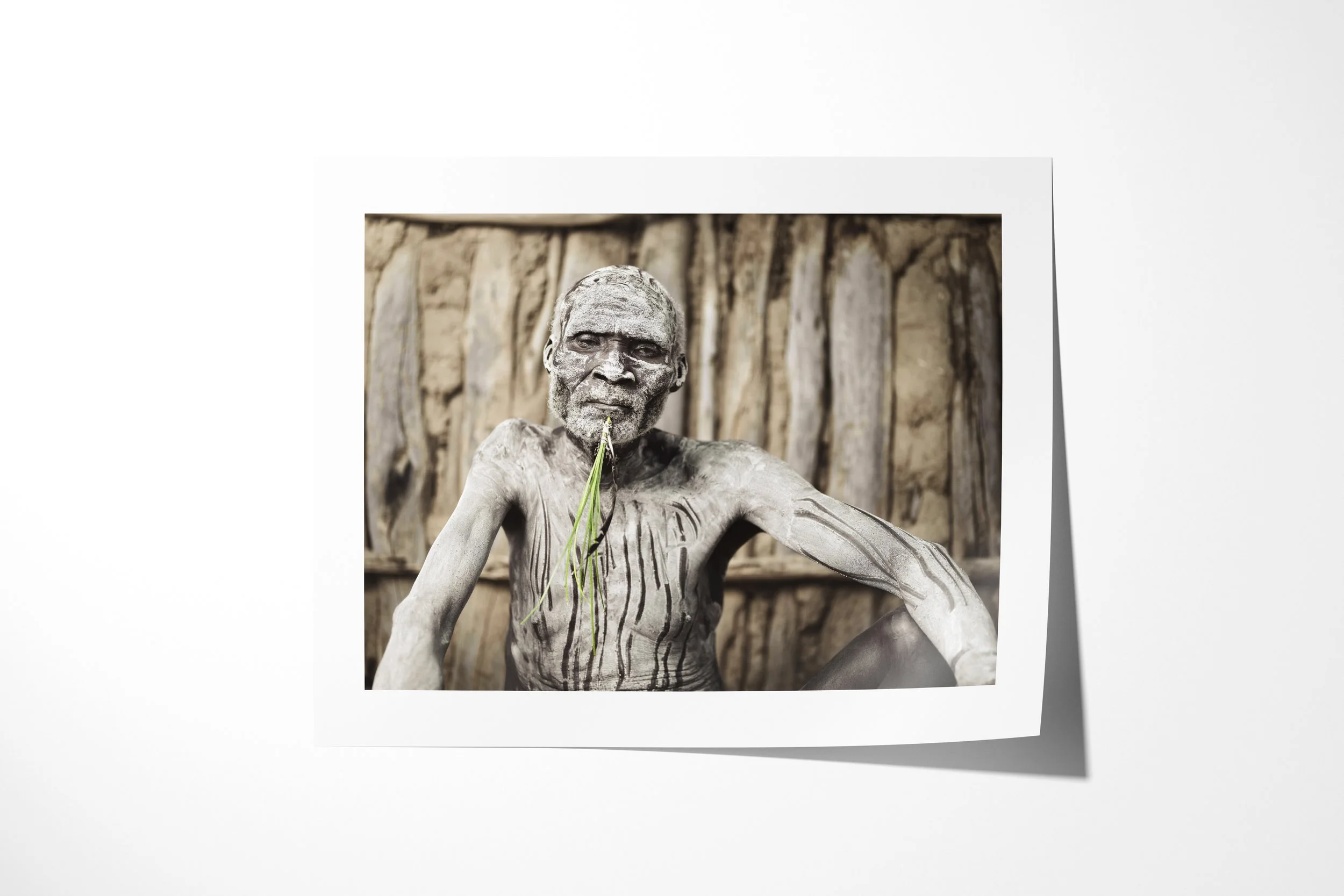 Fine art paper print of Bonko, showing an older Kara man with pale body paint and dark painted lines seated against a wooden wall.