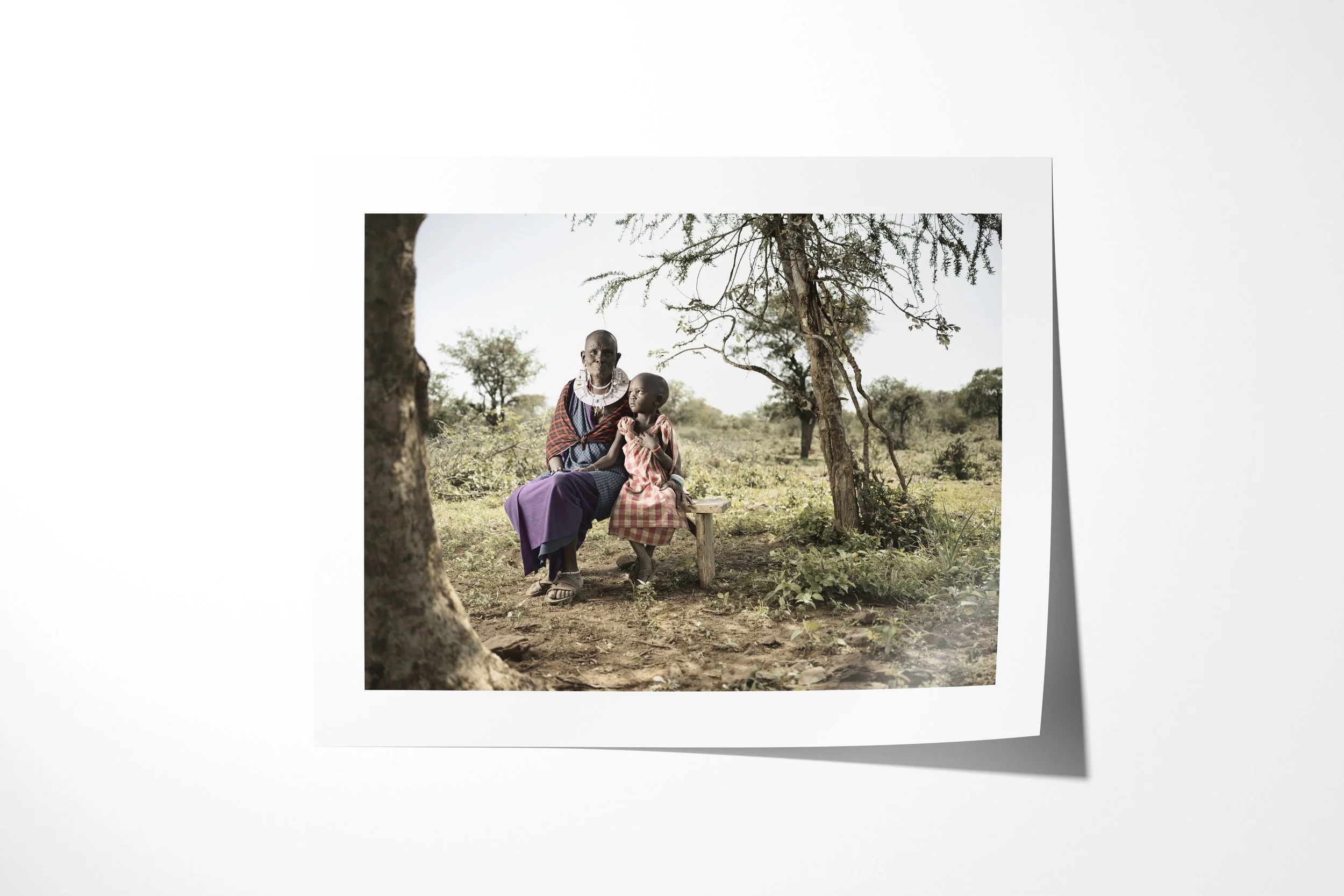 Fine art paper print of Naleku & Elias, showing Naleku seated beneath trees with her young grandson Elias standing beside her.