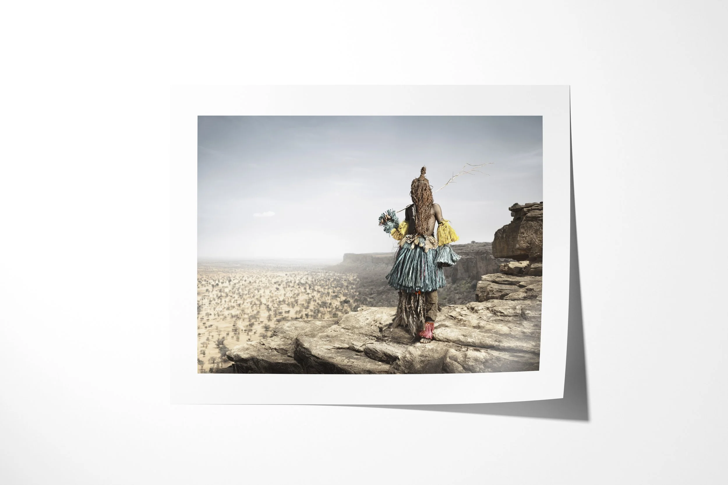 Fine art paper print of Benin Banin (Mask), showing a Dogon masked dancer seen from behind on a cliff overlooking the Bandiagara landscape.