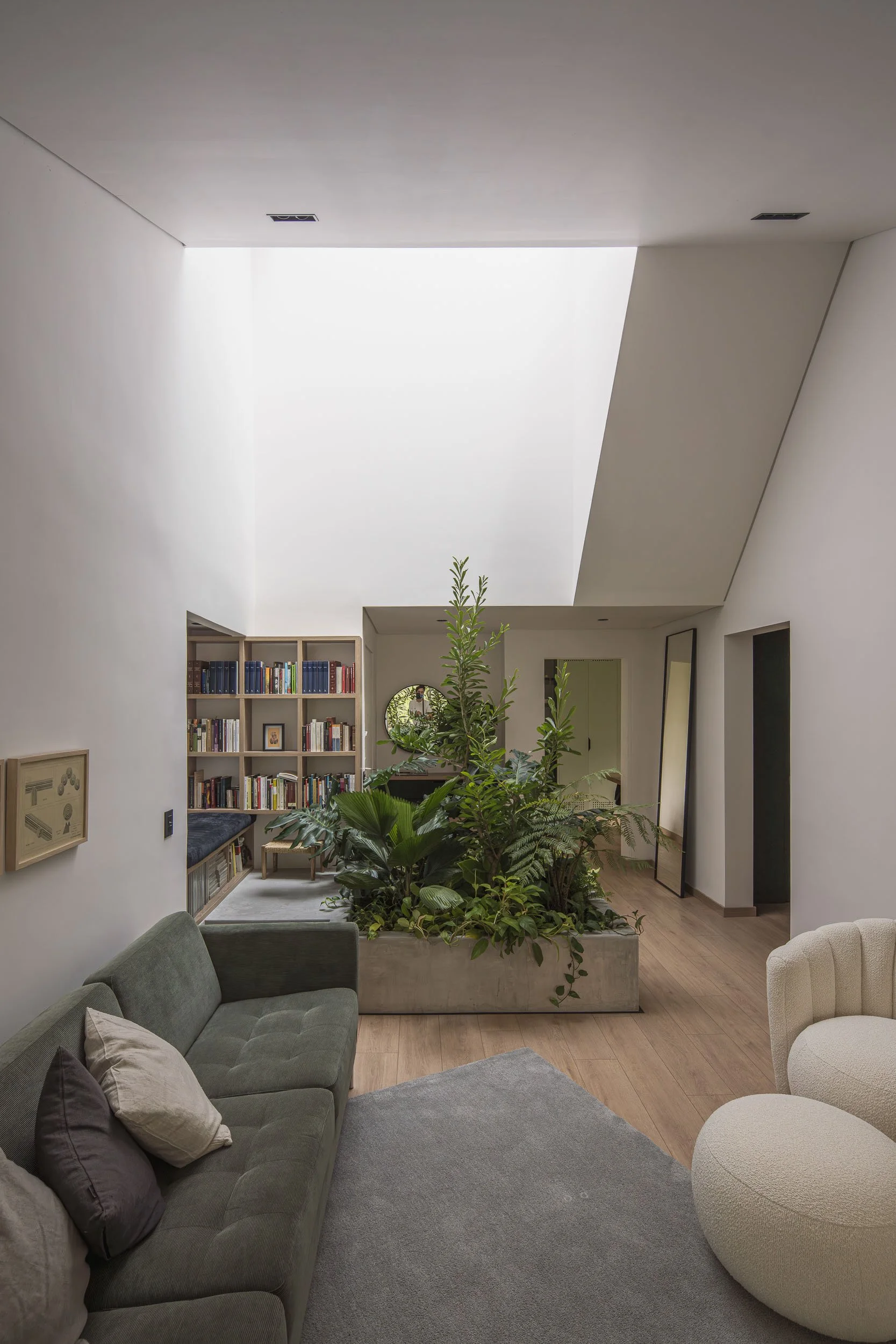 Salón moderno con una jardinera y rincón de lectura bajo un tragaluz grande. Muebles modernos en un espacio bien iluminado. Reforma del apartamento Guadalajara 602 en Medellín por TOLEDO Estudio de Arquitectura