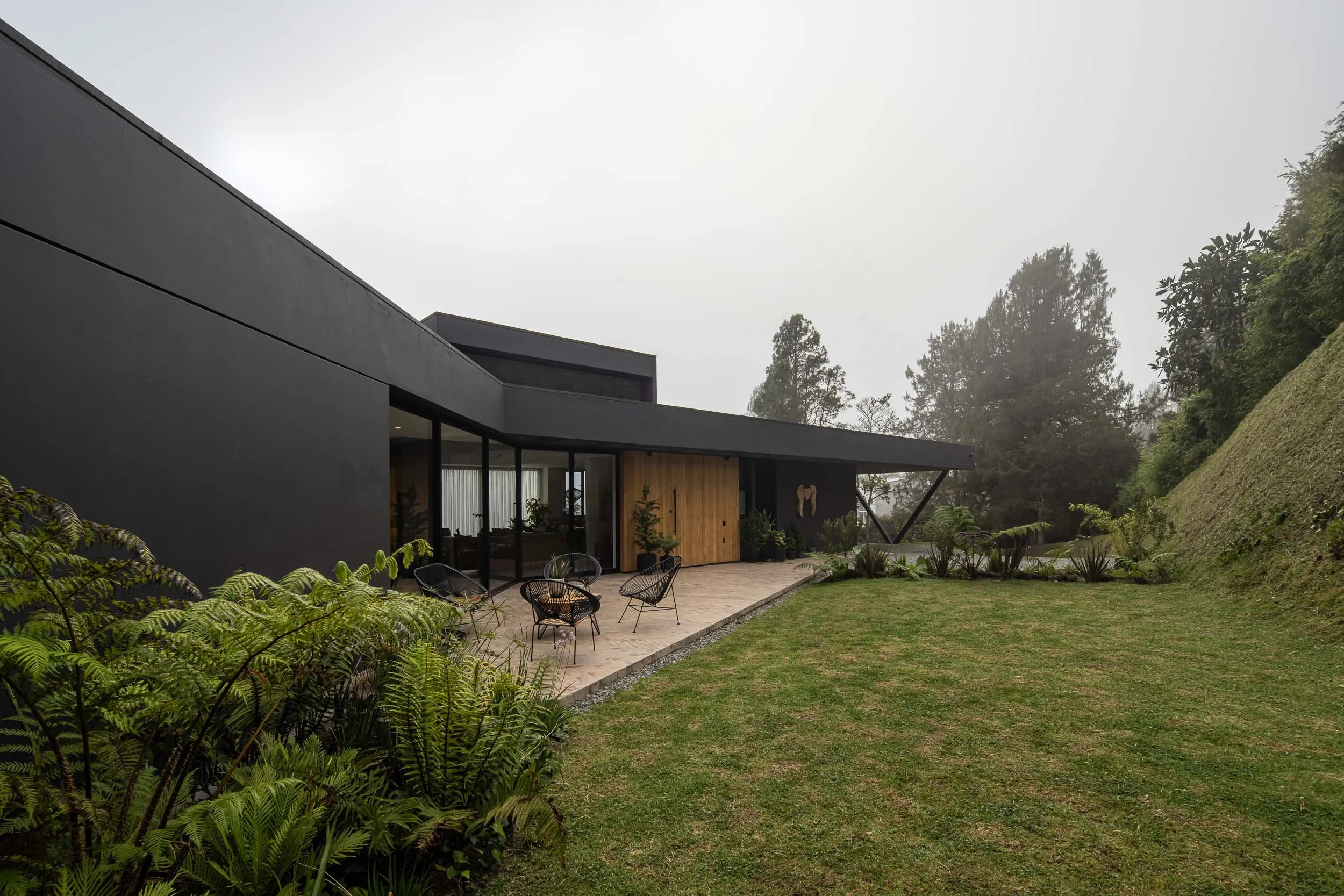 Casa JANA, una residenciacontemporánea con terraza y jardín verde, con plantas alrededor y árboles en la zona trasera, en un día nublado.