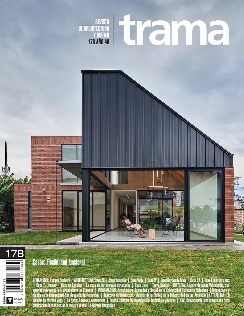 Portada de revista de arquitectura y diseño con una casa moderna que tiene un diseño funcional y flexible con estructuras de ladrillo y metal, grandes ventanales, una sala interior con sillones y una decoración contemporánea.