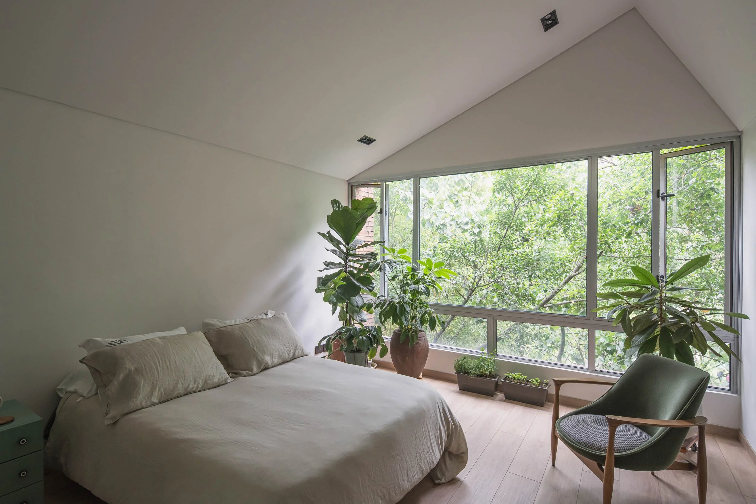 Habitación con techo alto inclinado y un ventanal que mira a los árboles en Medellín. Reforma por TOLEDO Estudio de Arquitectura en Guadalajara 602 en Medellín.