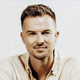 Portrait of a young man with short brown hair, light facial hair, and a neutral expression, wearing a beige polo shirt.