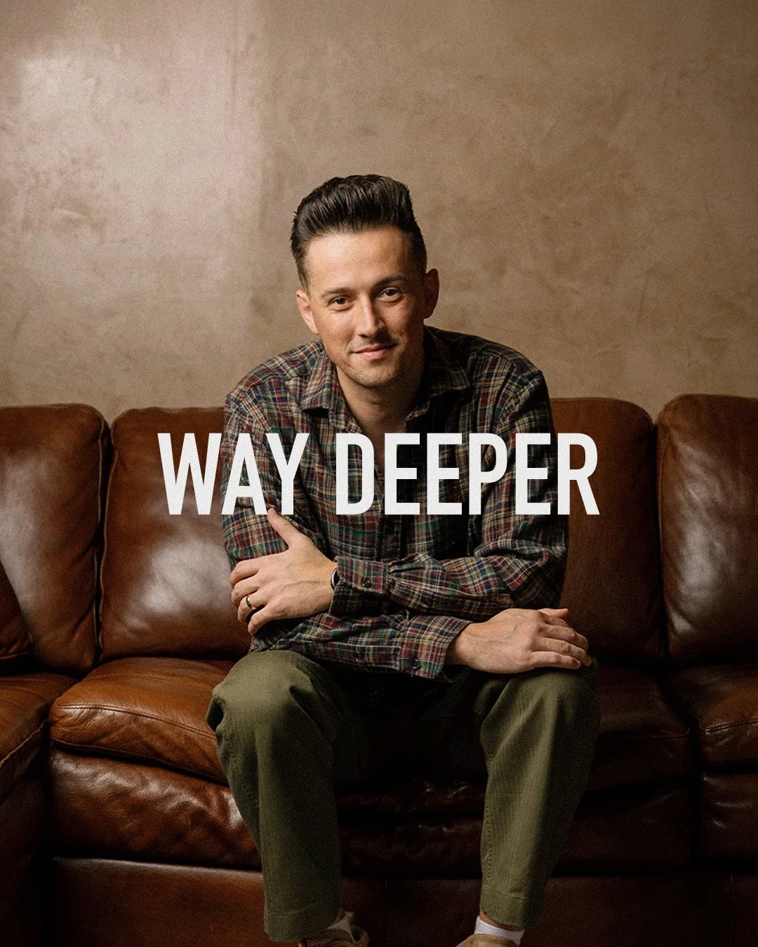 A man sitting on a brown leather couch, wearing a plaid shirt and green pants, with the words 'WAY DEEPER' overlaid.