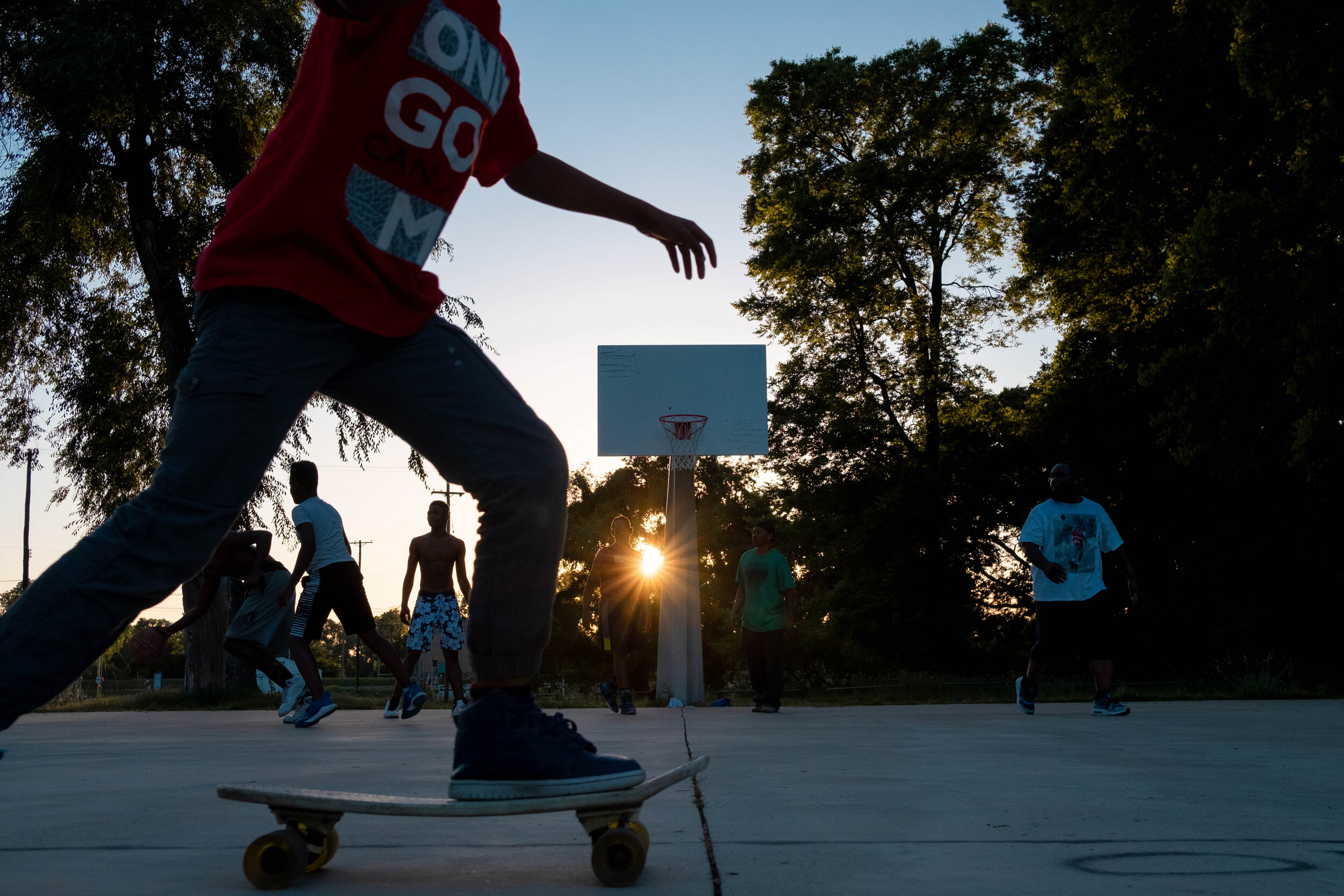  A boy rides by on a skateboard while young men play basketball in Booker T. Washington park.  