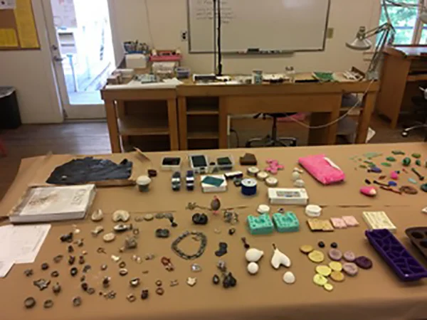 This is what the center work table often looks like at a casting workshop - covered in molds, samples, cast objects, wax, and books. (Awwww... it's CAST... thanks, Mary!) Photos below will zoom in on parts of this table. Photo courtesy of Mary Hallam Pearse.