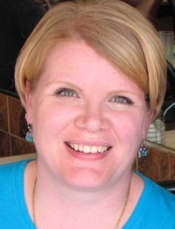 A headshot of a blonde woman smiling with blue earrings.