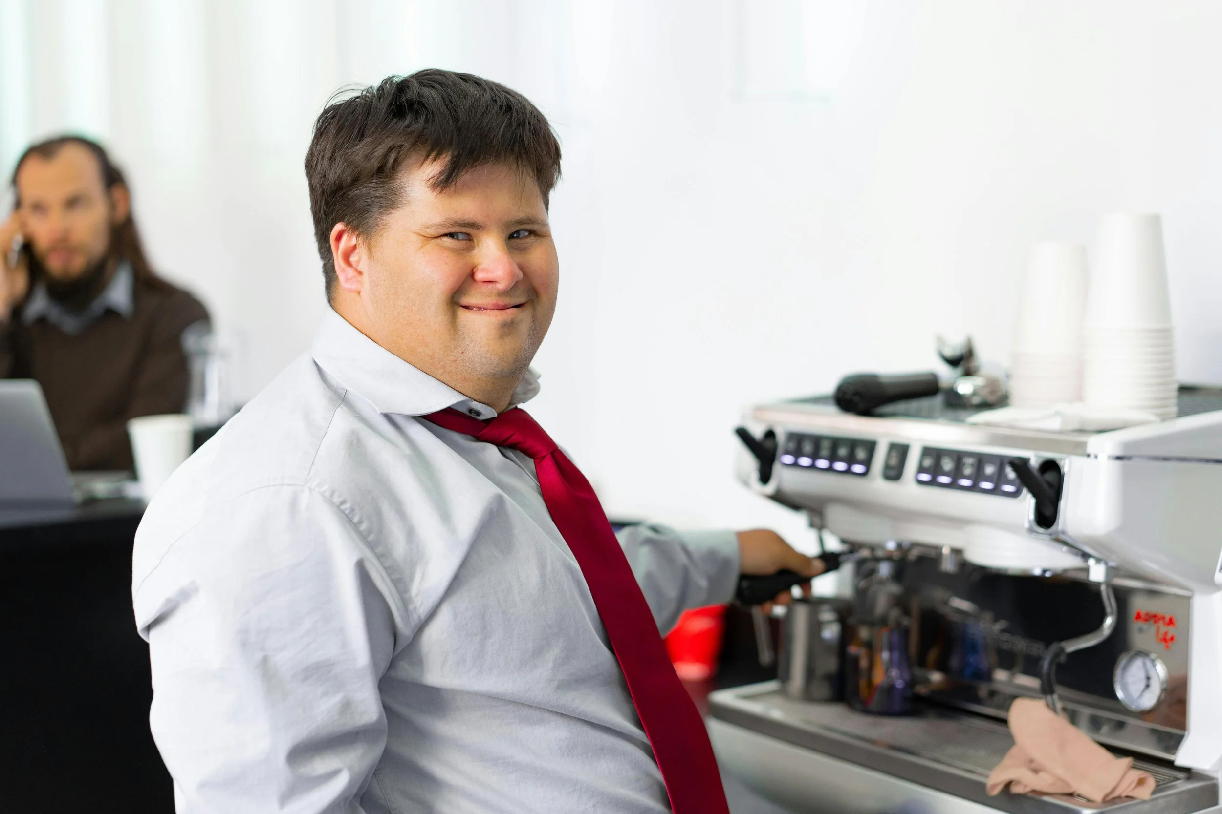 Smiling man in a white shirt and red tie preparing coffee at a café espresso machine.