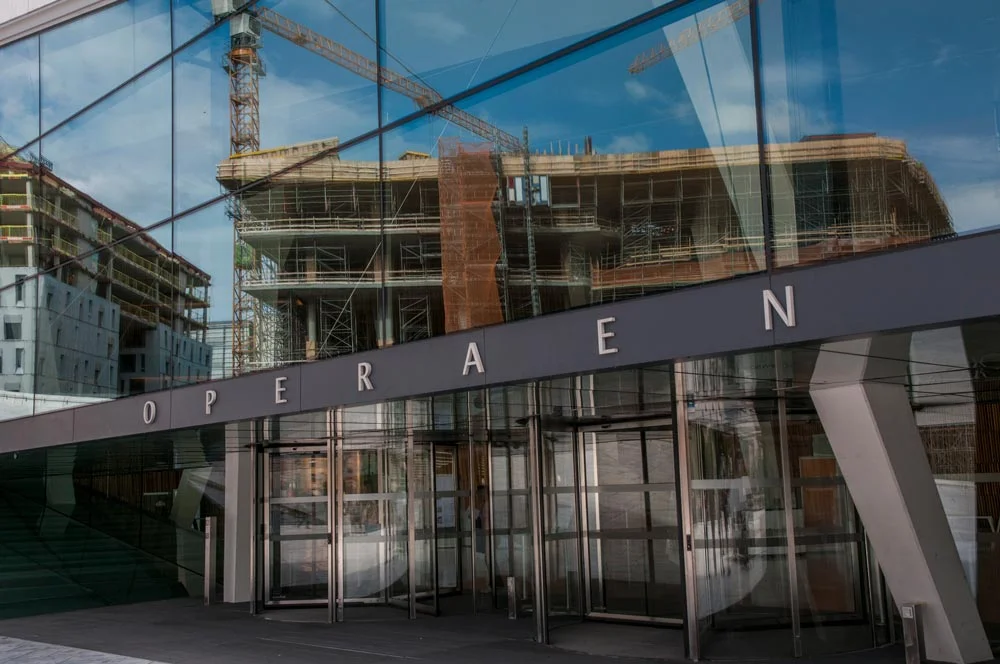 The entrance to the Oslo Opera House which is situated in Bjørvika harbour area of central Oslo with construction work reflected in the glass facade. ©Johan Siebke.