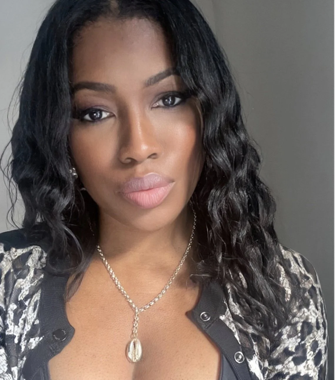 Paulina Elizabeth wearing cowrie shell necklace, with wavy relaxed 4c hair and leopard print top.