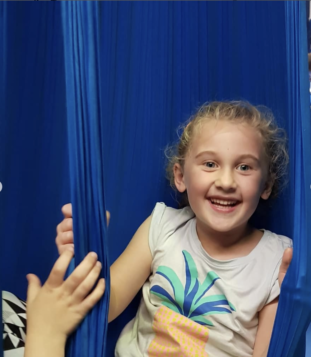 Young CircArts student smiling in an aerial silk hammock