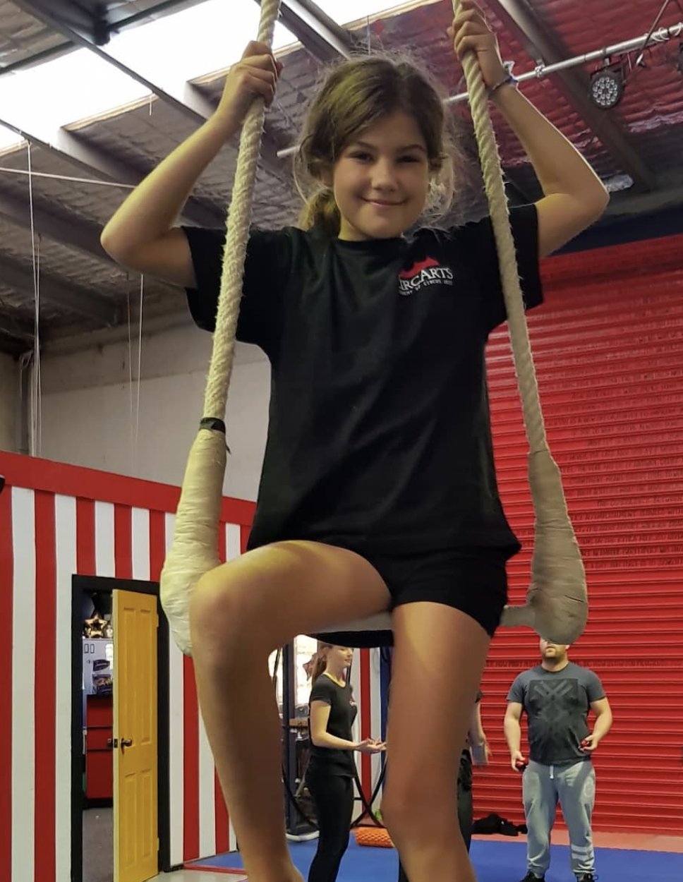 Teen sitting on a static trapeze in the CircArts studio