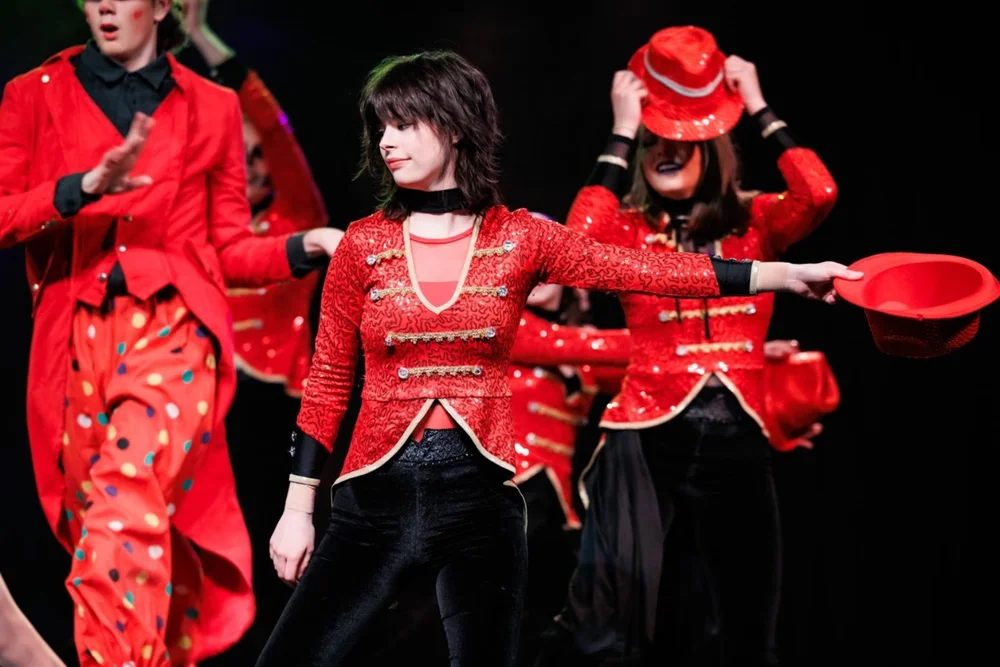Teen performers in red sequin costumes dancing a hat routine together on stage