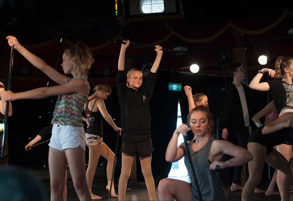 A group of young dancers learning a routine with dance sticks in rehearsal