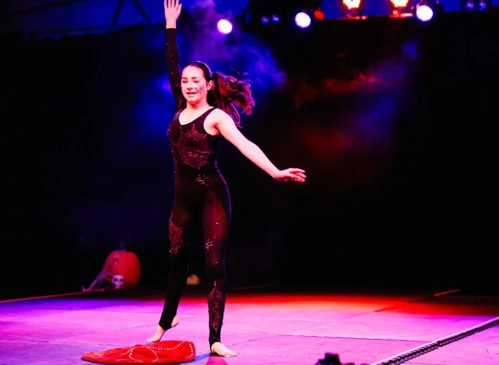 A teen performer dancing across the stage with one arm raised under coloured lights