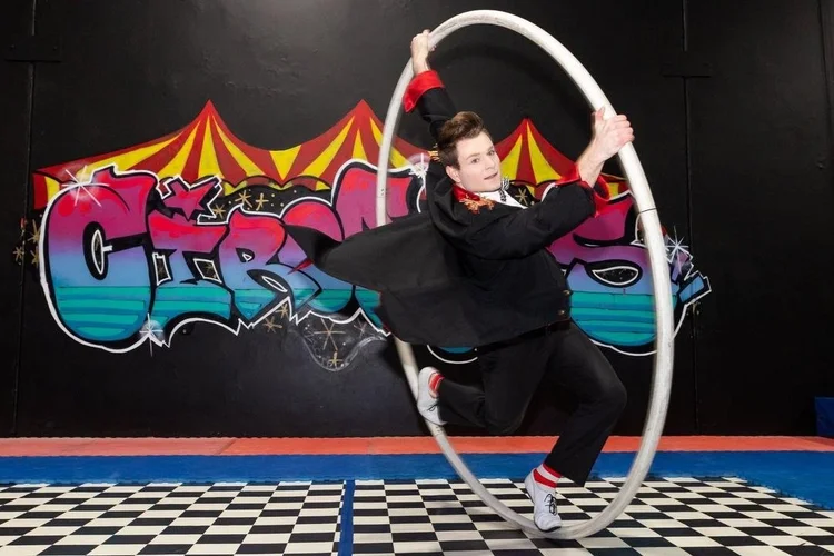 Coach balancing inside a cyr wheel in front of the CircArts mural