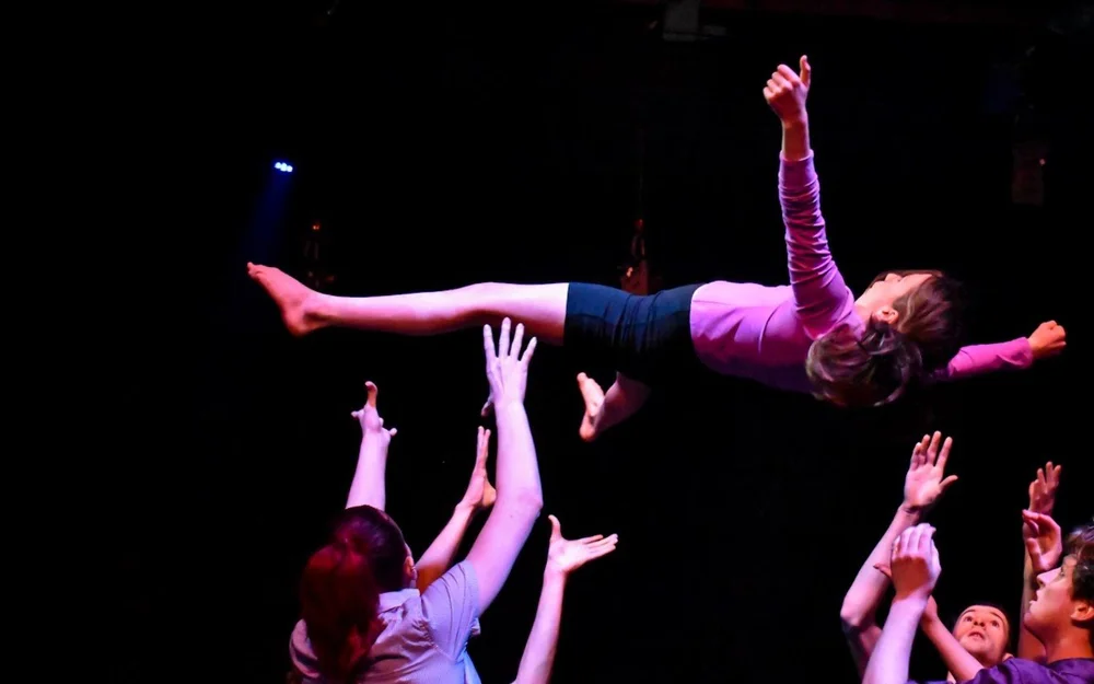 CircArts teen performers throwing a flyer high into the air on stage
