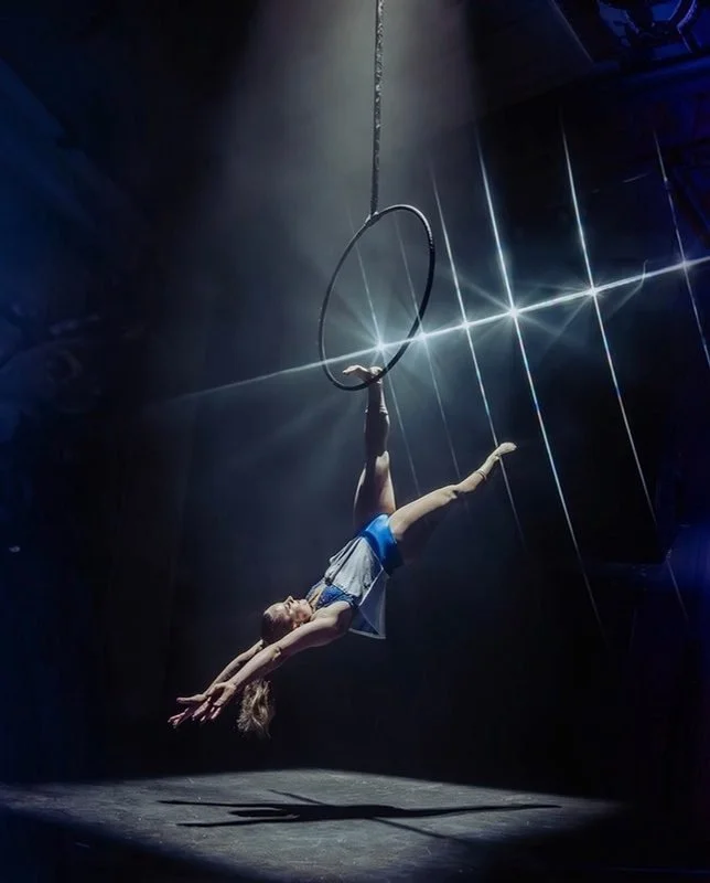 Charli Meath hanging from an aerial hoop under a spotlight