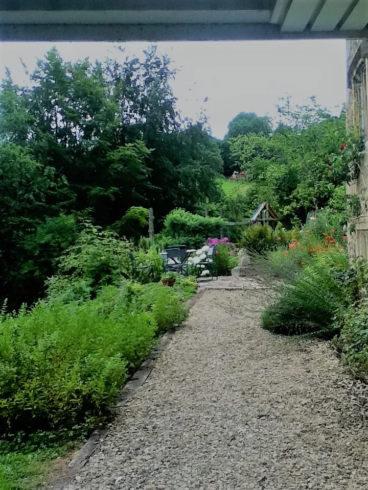 Reinstated gravel path between full borders, leading to a seating area