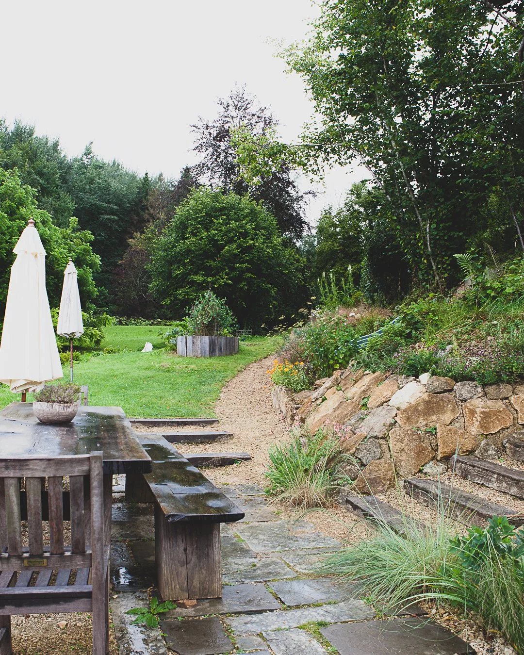 Paved seating area with a long timber table and benches beside terraced stone walls