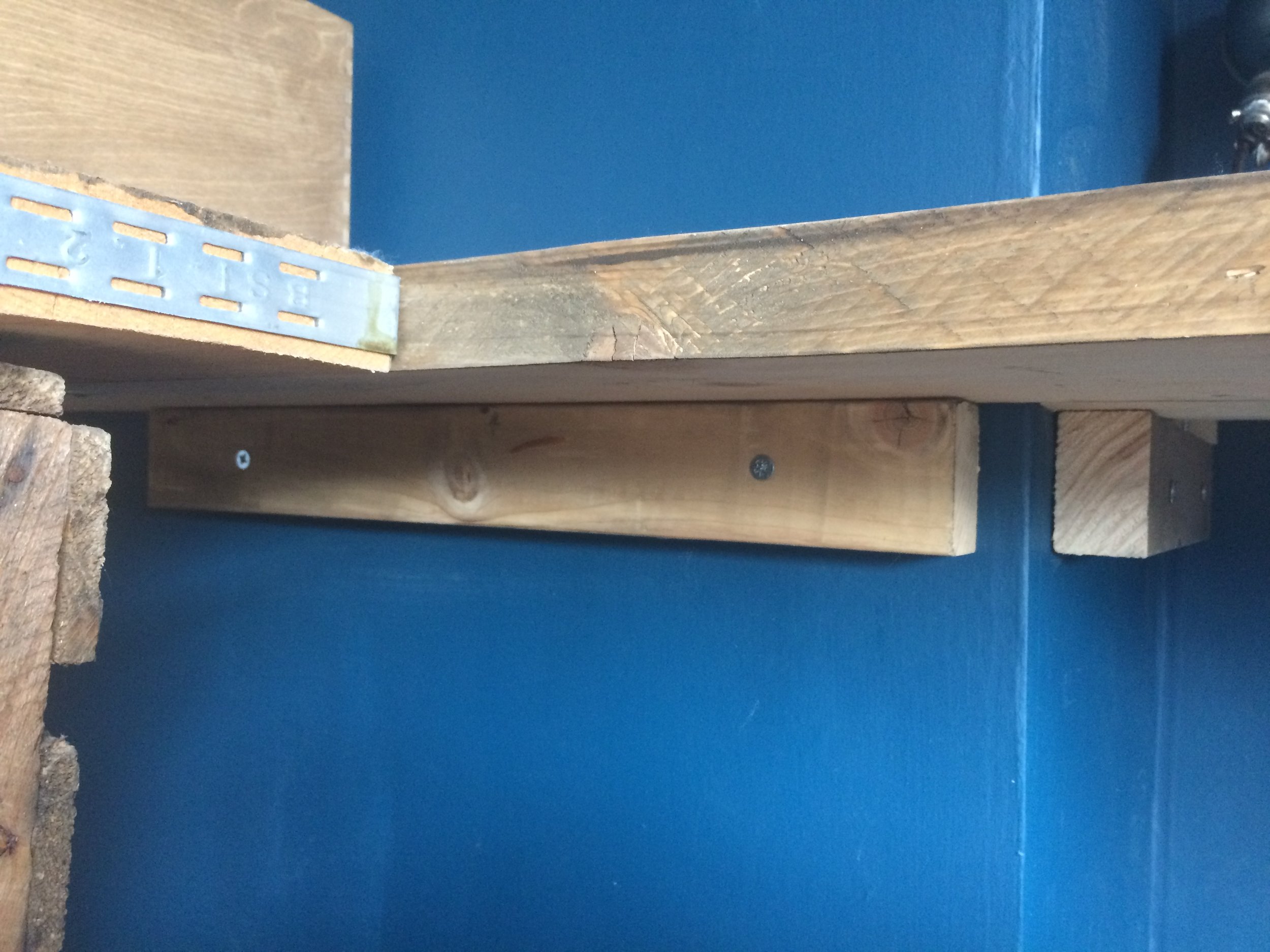 Battens of wood attached to the wall supporting the back board. The front two boards are supported by the crates.