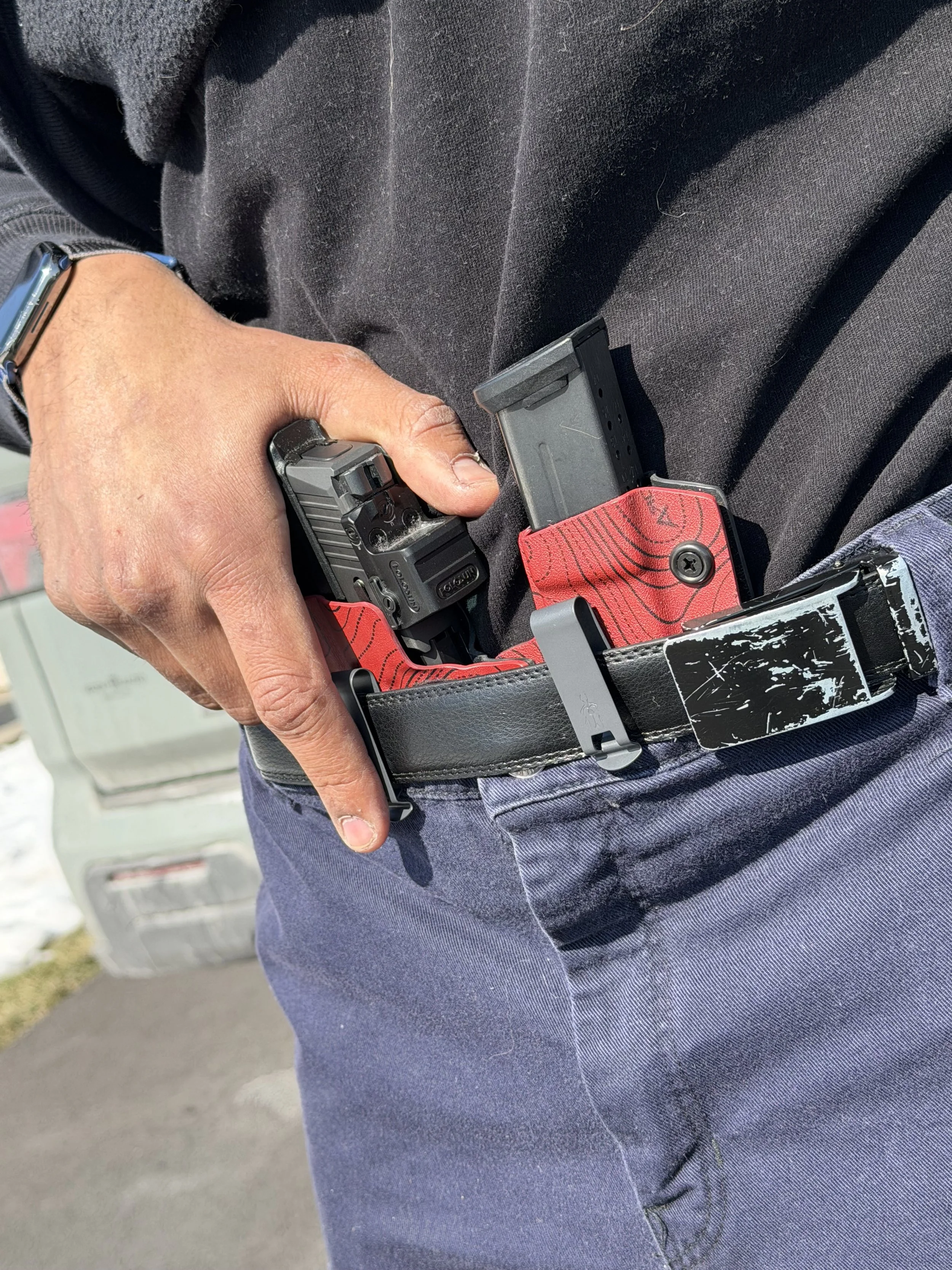 Person holding a gun with a magazine while wearing dark clothing and a red holster.