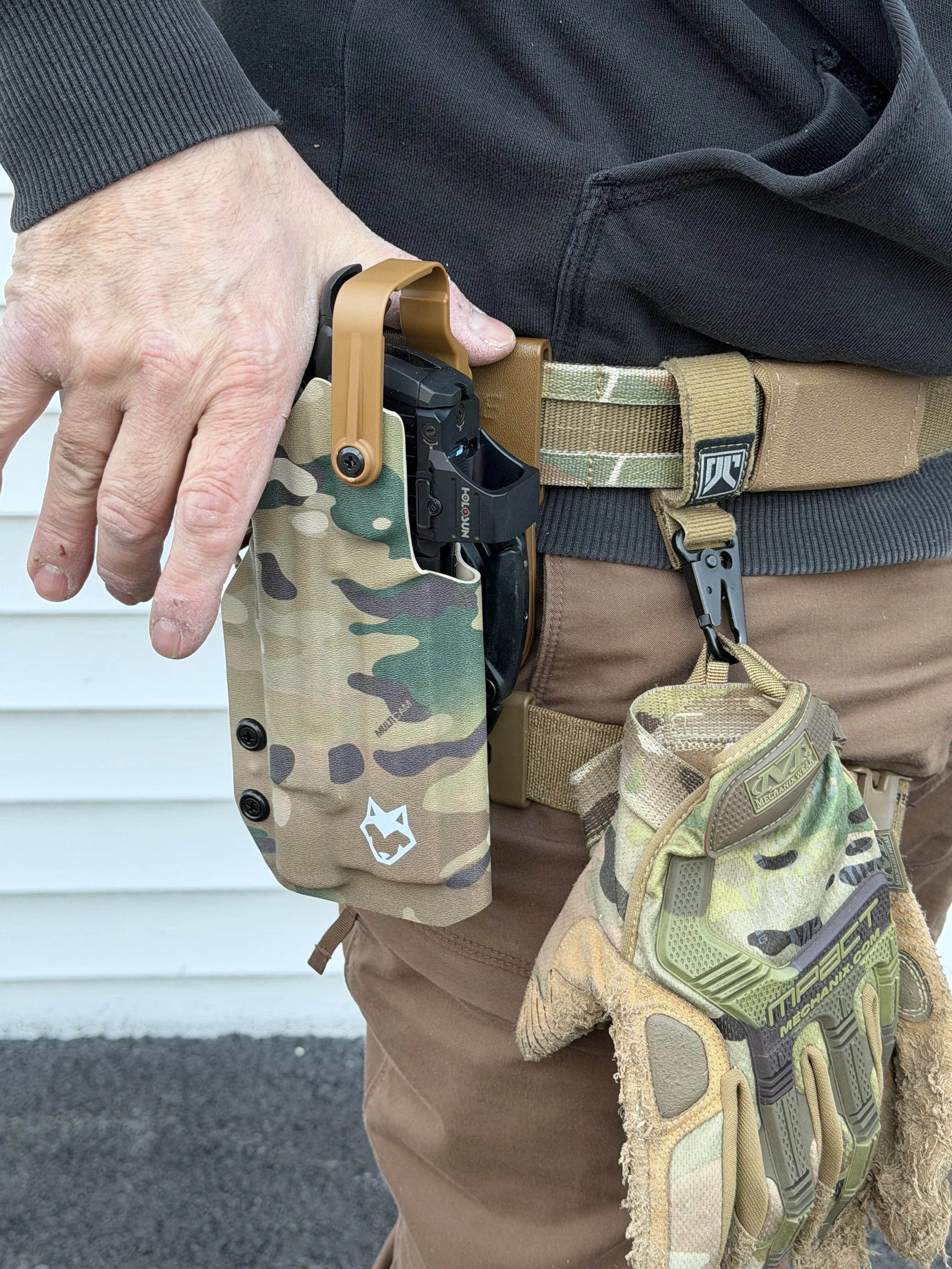 Close-up of a person dressed for tactical or outdoor activities, wearing a black shirt, tan tactical pants, a camouflage belt, and a tactical thigh holster with a firearm secured in it.