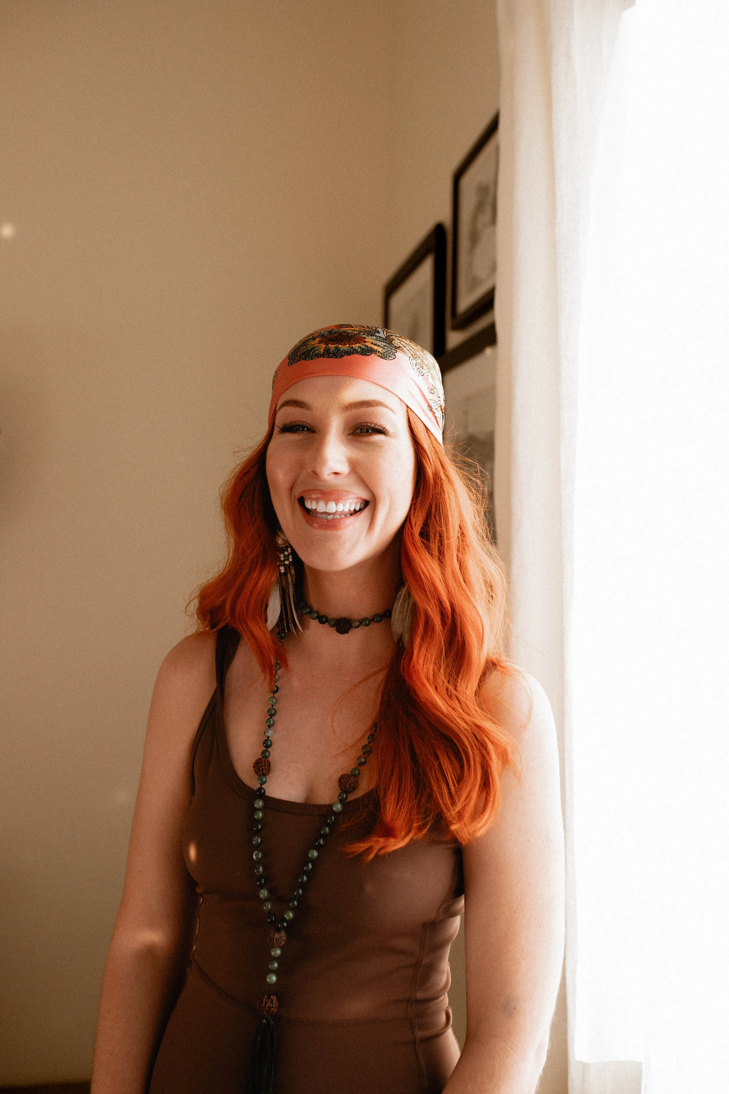 Mary- A woman with long, wavy red hair, wearing a pink headscarf and a brown tank top, with a beaded necklace and earrings.