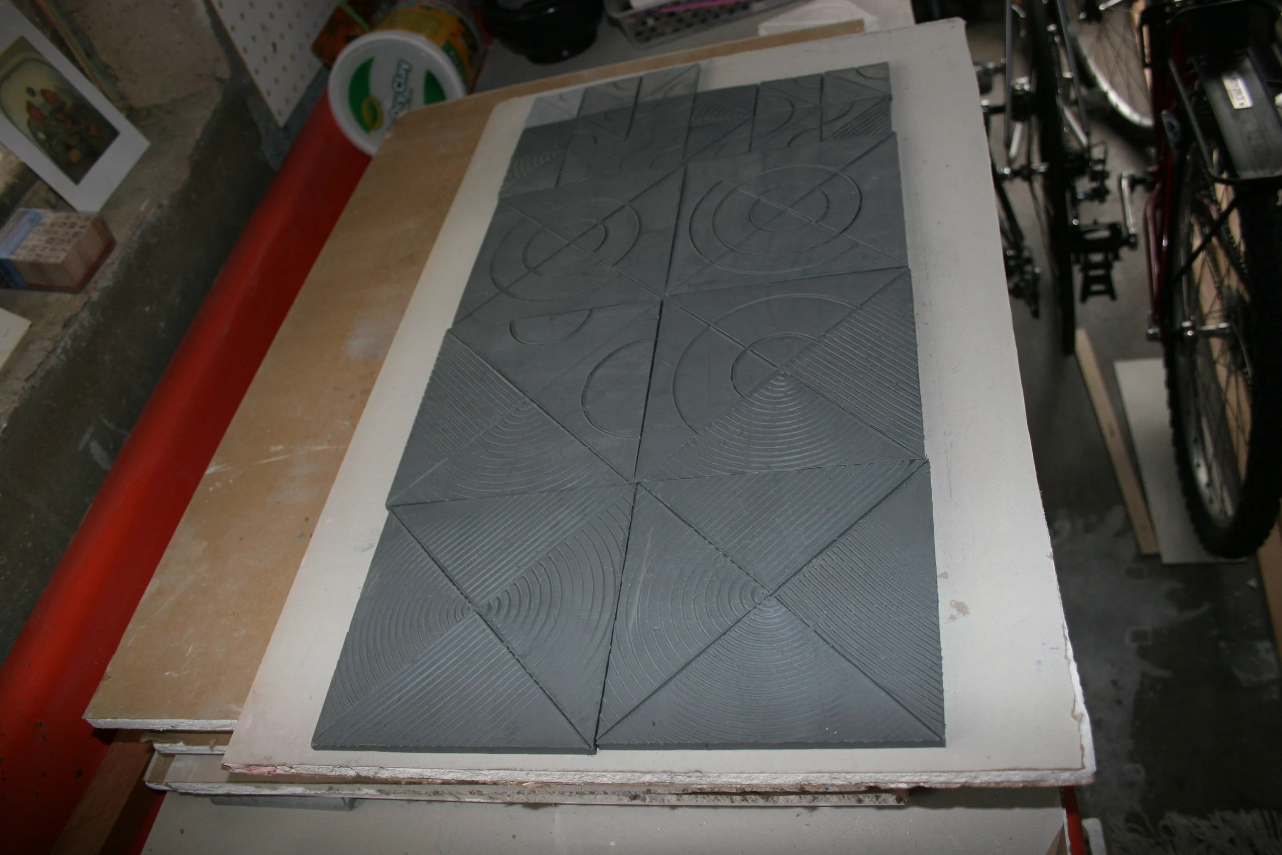 After rolling the clay into a large flat slab, I cut it into squares. After they have dried to a leather hard state, I incise the designs into each tile.