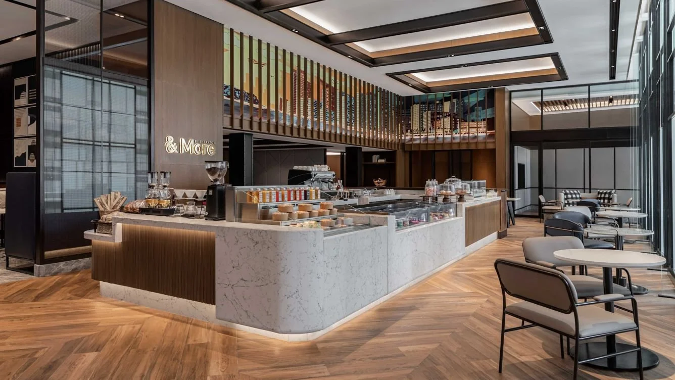 Modern cafe interior with a marble counter, seating area with tables and chairs, and a wooden-floored space with large windows.